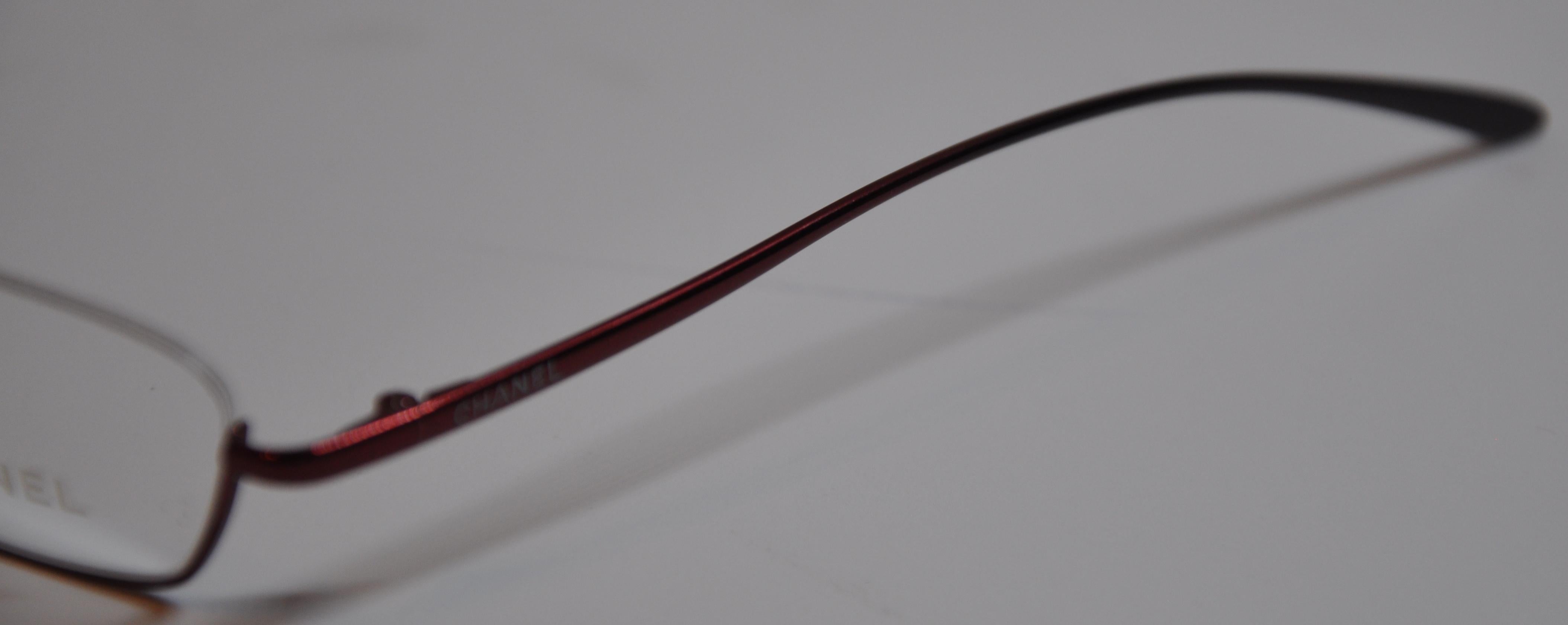   Chanel wonderfully elegant titanium iridescent cranberry-red weightless reading glasses is detailed with curved corners on the front as well as streamline curved arms. The front measures 5 1/8 inches across, height is 1 inch, and the arms measures