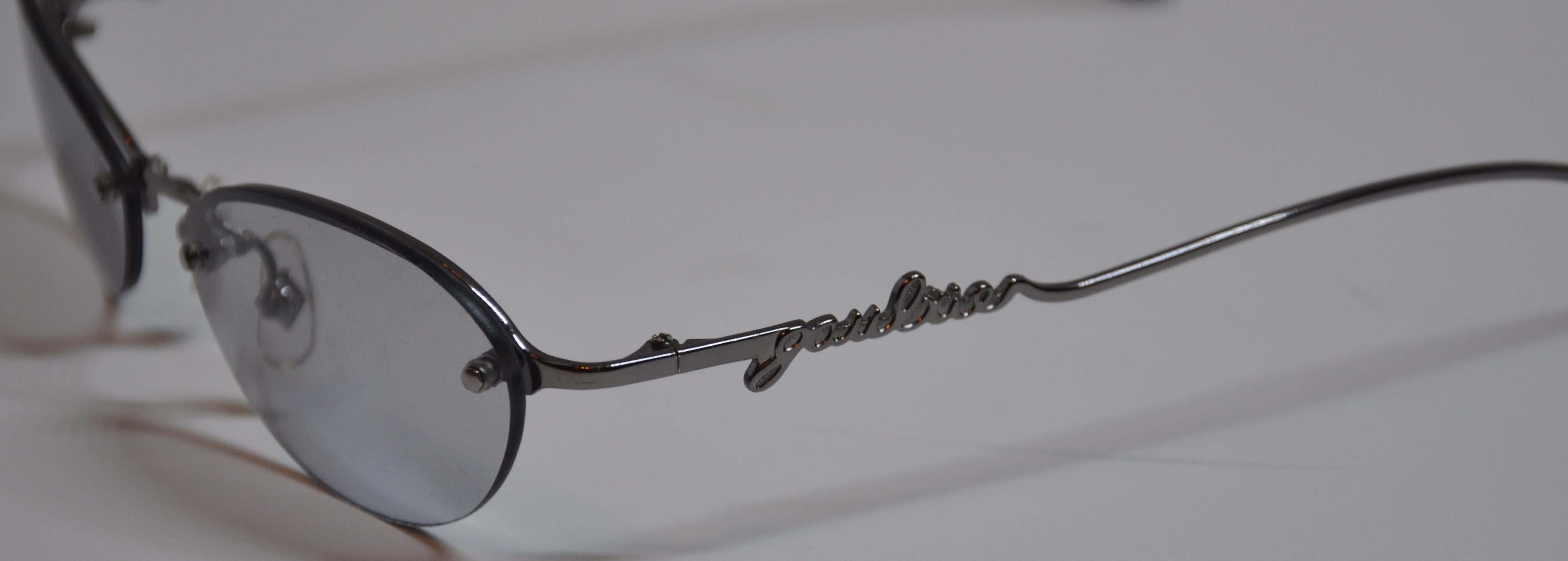 Montures en argent doré de Jean Paul Gaultier accentuées par le nom de la signature en script sur les deux branches de ces lunettes à verres correcteurs. Le pont est orné de JPG et l'avant est rehaussé de clous de quincaillerie argentés. La longueur