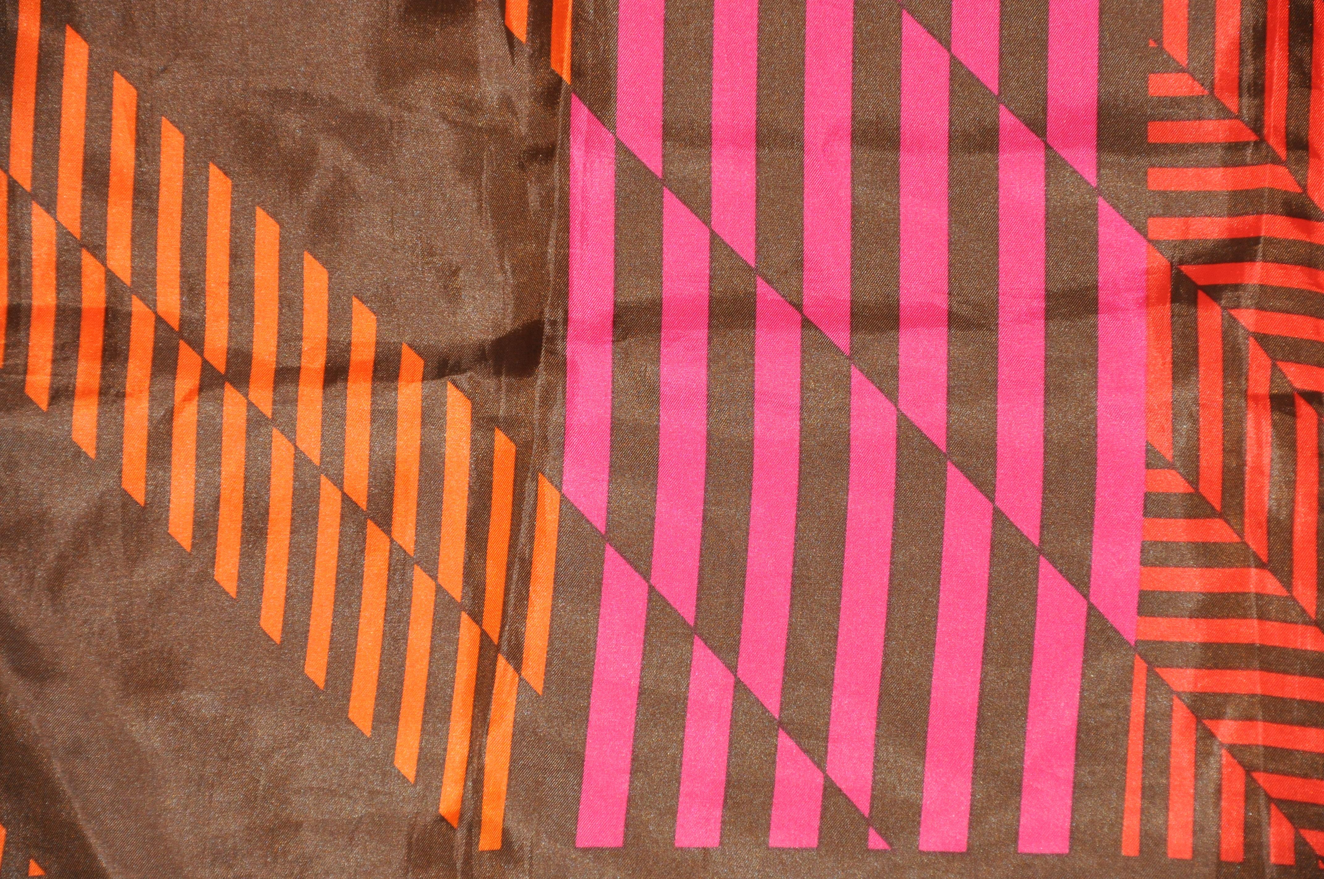        Whimsical coco brown borders surrounding abstract tangerine & fuchsia stripes polyester scarf measures 26 inches by 27 inches, and finished with rolled edges. Made in Japan.