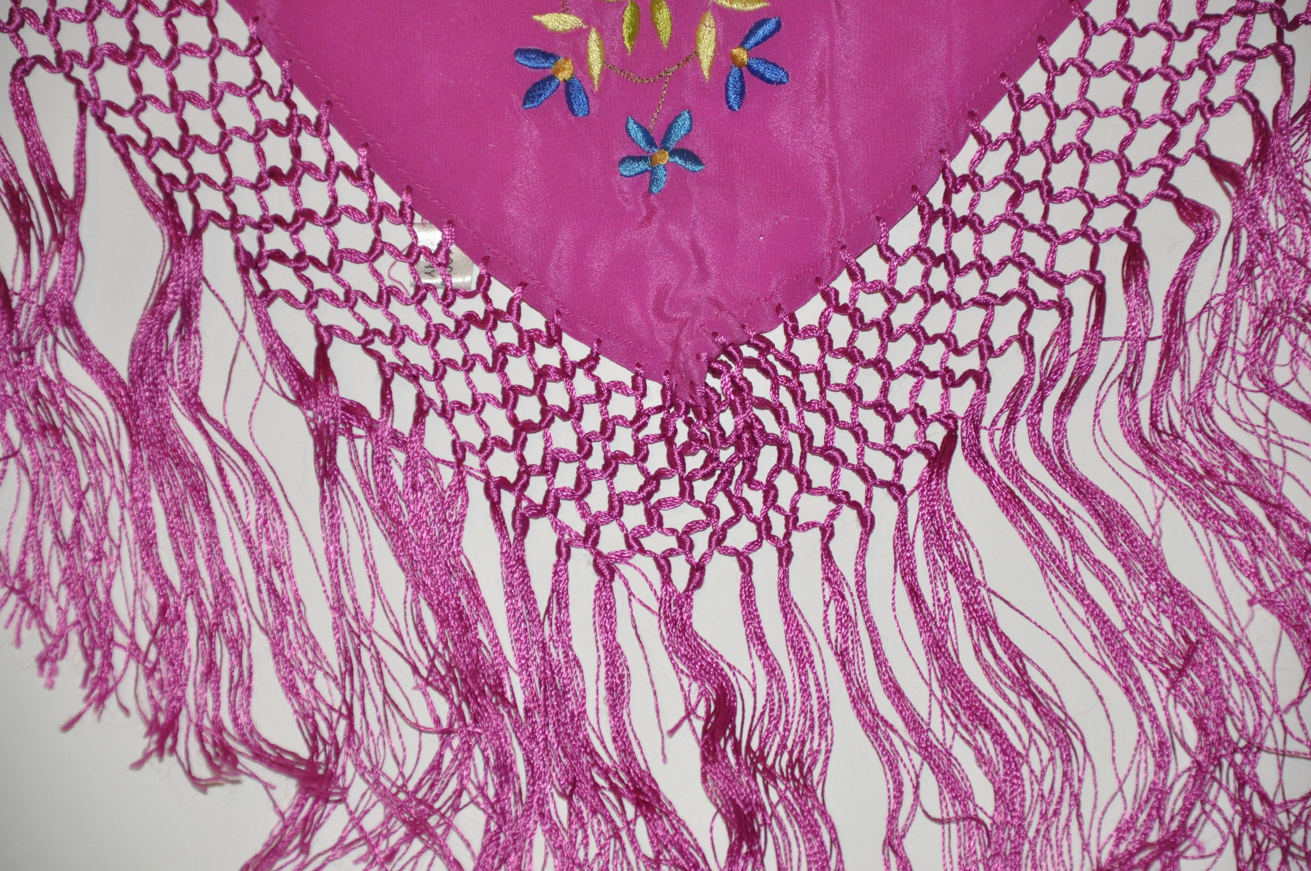        Ce magnifique foulard en soie fuchsia est orné d'éclats de fleurs multicolores brodées à la main de plusieurs tailles. Il est rehaussé d'un cordon de soie à plusieurs niveaux noué à la main qui souligne la frange mesurant 15 cm de long. Le