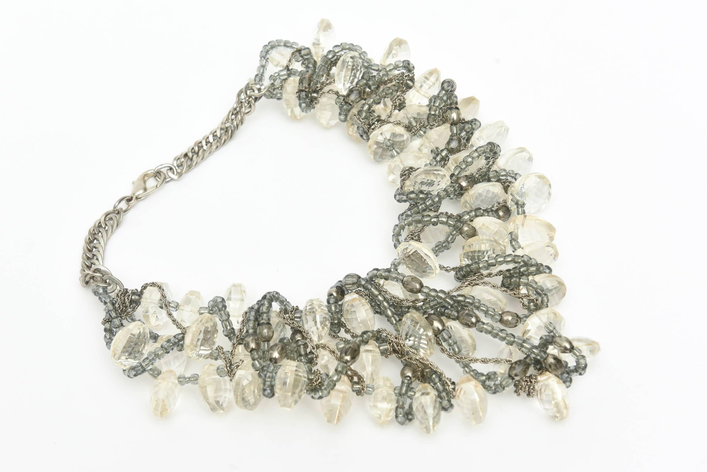 This most arresting and unusual bib chunky multi strand necklace is from the 80's. It is faceted clear lucite interspersed with intertwined chain, gray beads and silver. It is rock star meets elegance meets very chic and cool.  It is a conversation