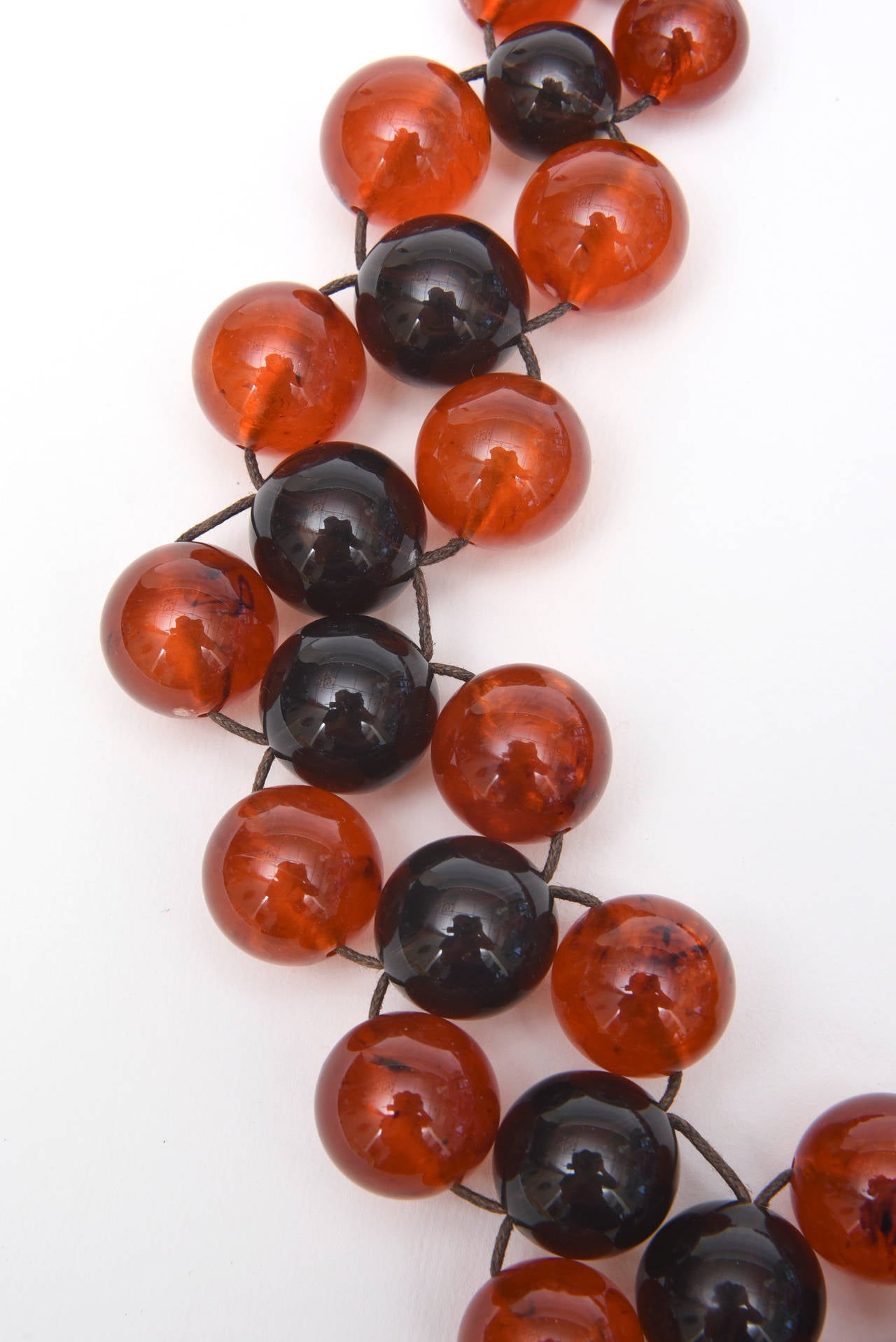 Des boules d'ambre orange et de résine violette noire rendent ce collier vintage amusant et attrayant.  Il est monté sur un fil et relié à trois rangées en quinconce. Les couleurs sont parfaites pour toutes les saisons Au Courant ! Nous offrons