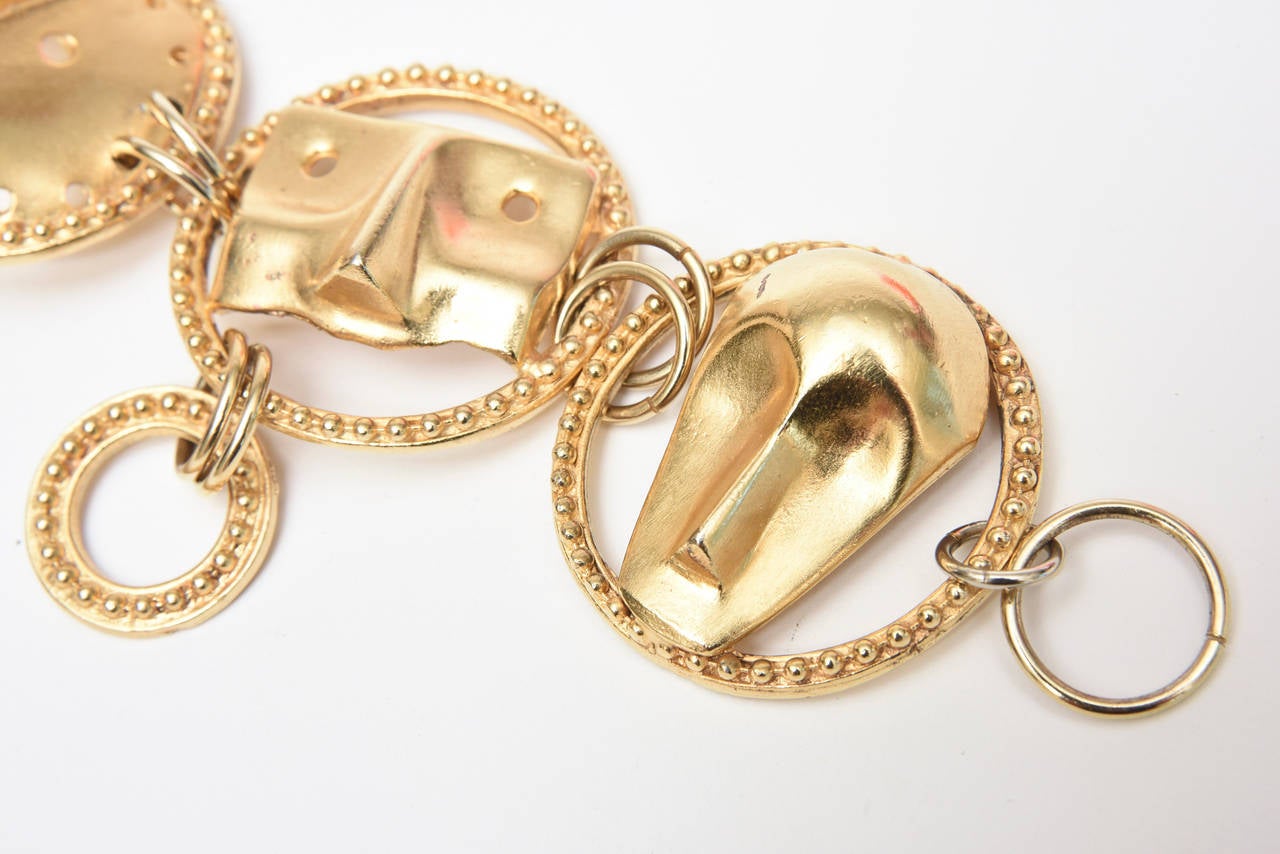 This unusual link gold plated bracelet has 4 abstract face masks. There is one disk that has a round beaded circle hanging. The beads encompass each disk. It is signed by a Japanese artist: Yo Hai. It resembles a charm bracelet and is from the 90's.