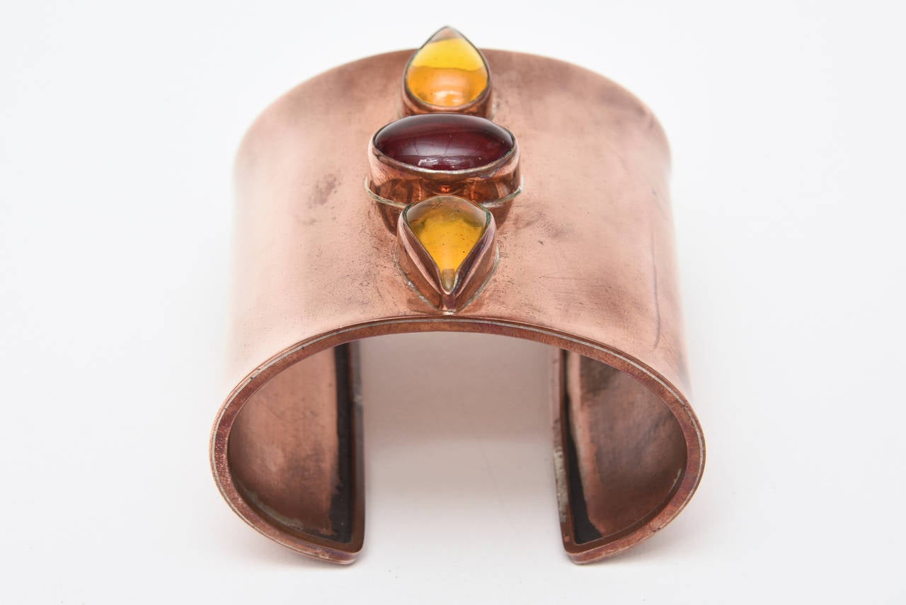 Dieses auffällige breite Armband aus Kupfer und 3 Glassteinen ist ein wahrer Blickfang am Handgelenk. Es hat 2 gelbe, bernsteinfarbene, tropfenförmige Gläser und ein längliches, rotes Glas. Die Punzierungen im Inneren haben einen tierähnlichen