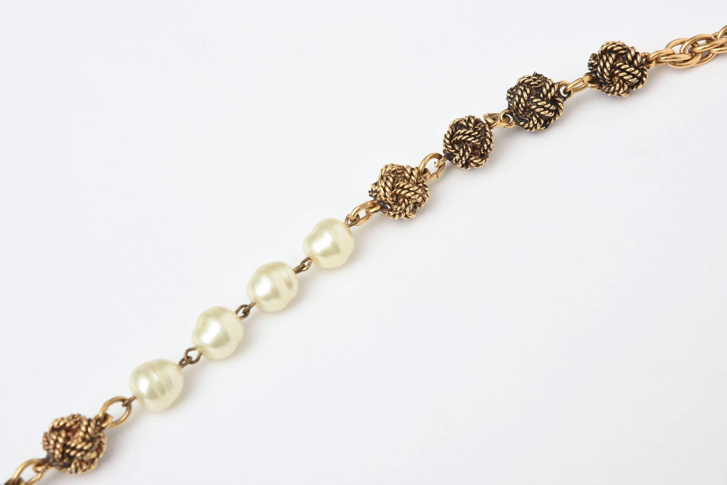 This classic and forever Chanel long necklace has knots in a darker gold plated gilt metal with a lighter gold plated gilt metal link interspersed with gold tone love knot stations interspersed with Chanel nacre faux pearls and chains. It can be