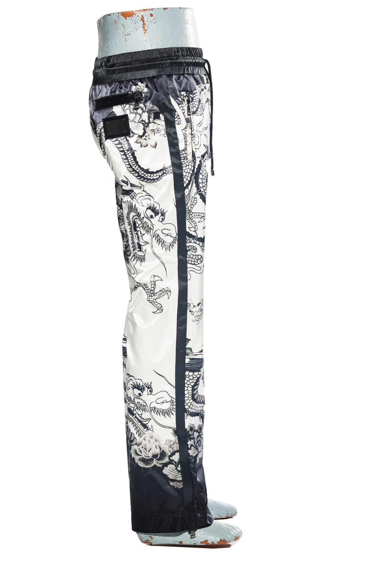 Dolce and Gabbana, Spring-Summer 2009 printed satin pants with dragon motif, zippers at ankles, silver-tone logo plate at back, three zip pockets, drawstring waist and front fly closure.

Retail $1745

Waist 31”, Hip 38”, Rise 10.5”, Inseam 33”, Leg