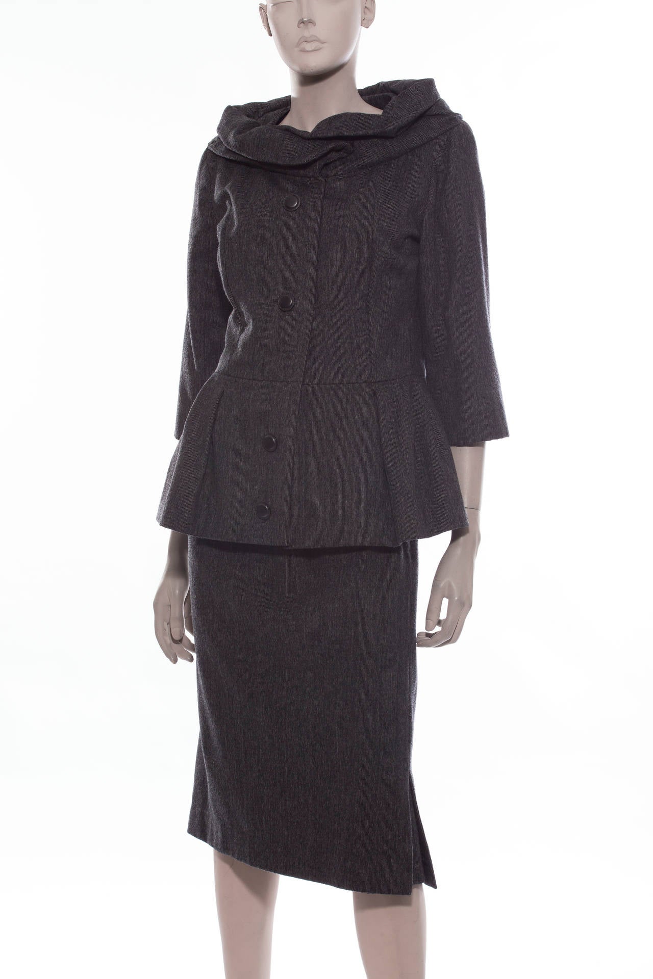 Christian Dior, circa 1960s charcoal grey wool skirt suit.Jacket is fully lined with four buttons,3/4 length sleeves,shawl collar and peplum. Skirt has side zipper,two kick pleats and fully lined.