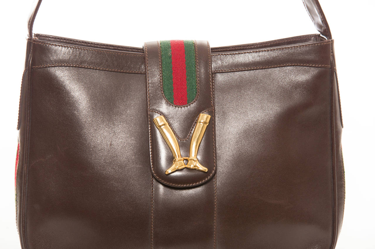 Gucci, circa: 1970's chocolate brown leather handbag with gold plated  equestrian boots on the fold over adjustable shoulder strap,tan leather interior with one pocket and gold zipper Gucci pull.

Height 9, Width 12, Depth 2.5, Shoulder Strap Adusts