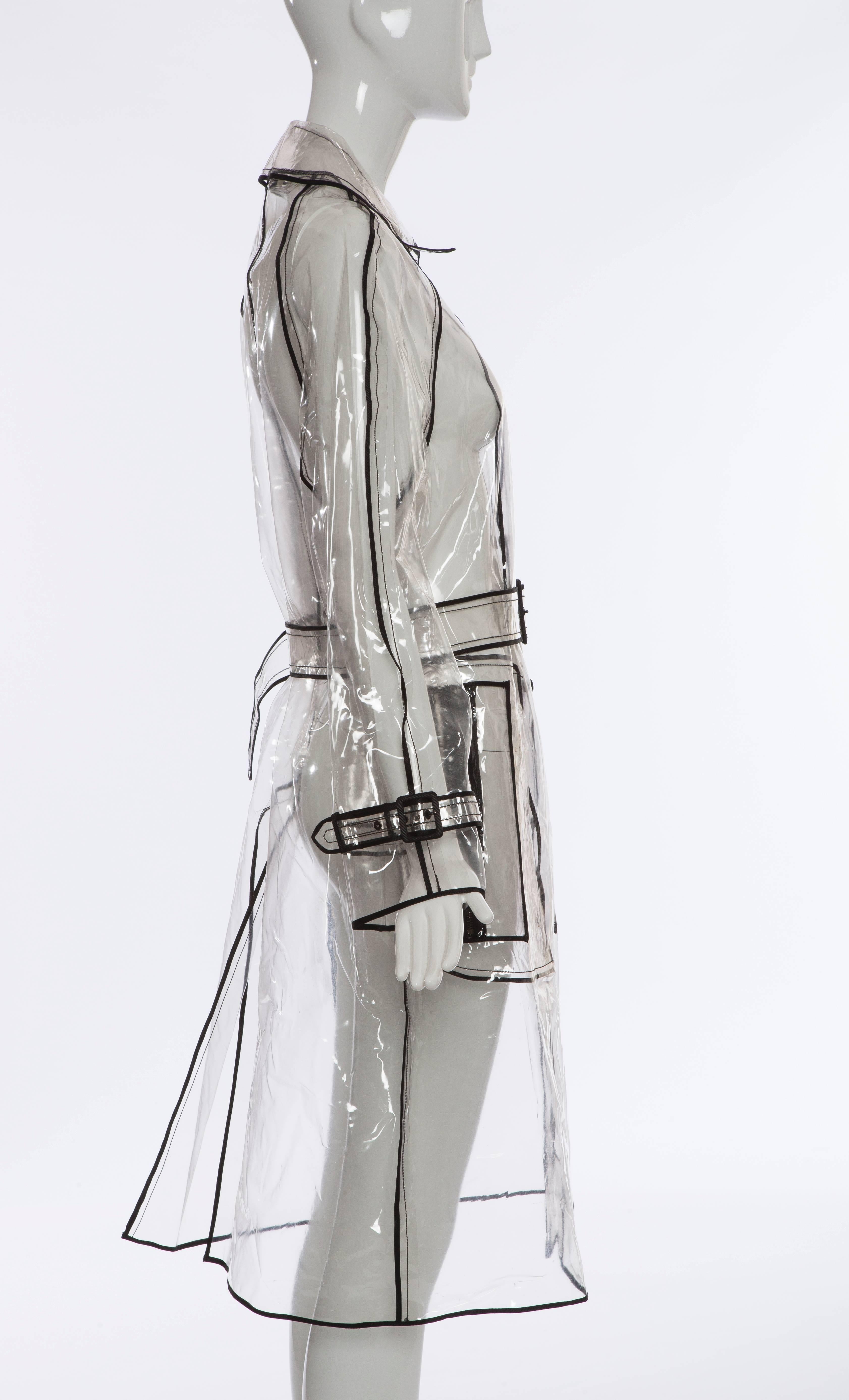 Prada, Autumn - Winter 2002-3, transparent PVC rain coat with pointed collar, long sleeves, dual zip pockets at sides, belted waist, contrasting black trim throughout and snap closures at front. 

Exhibited at the Met's Spring 2012 Costume