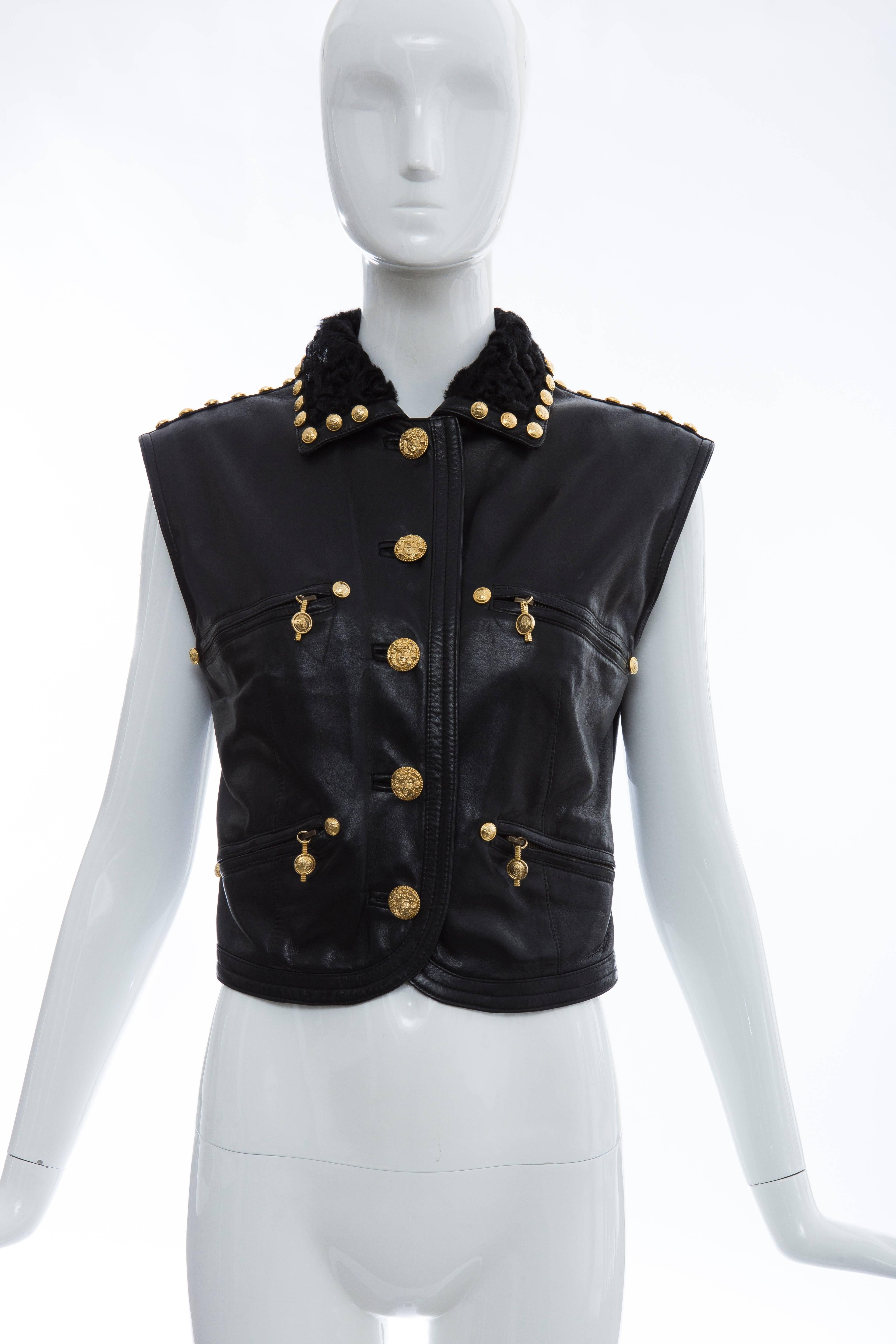 Gianni Versace, circa 1990's, black leather cropped vest with Persian lamb collar, gold-tone Medusa stud embellishments at collar, shoulders and center back, four zip pockets, Medusa button closures at center front and fully lined.

Size: