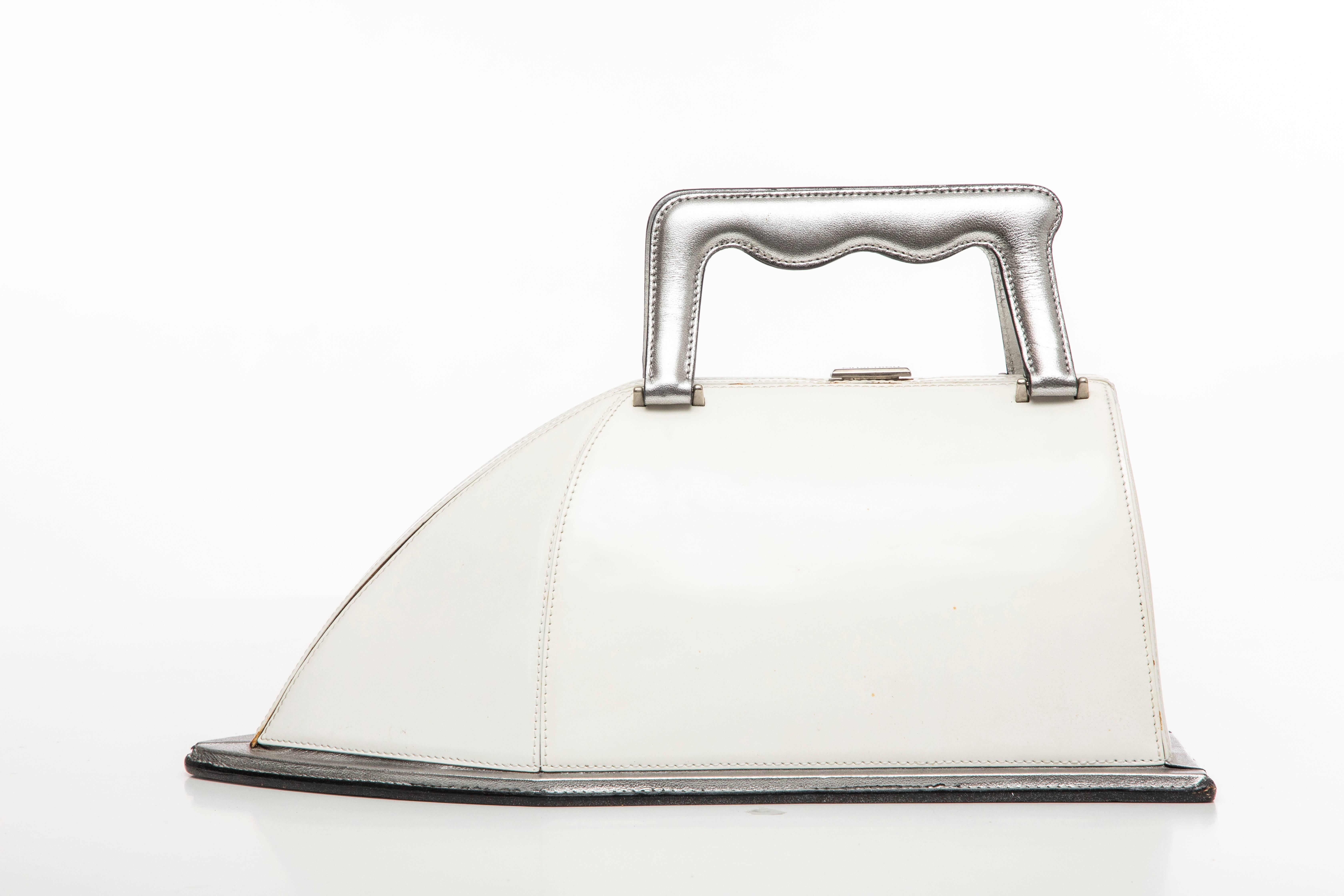 Moschino, circa 1995 white lacquered leather iron handbag with dual silver flat top handles and trim and aluminum hardware, dual flat top handles, black woven lining and push-lock closure at top.

Handle Drop: 2.5, Height 5.5, Width 12.5, Depth 6
