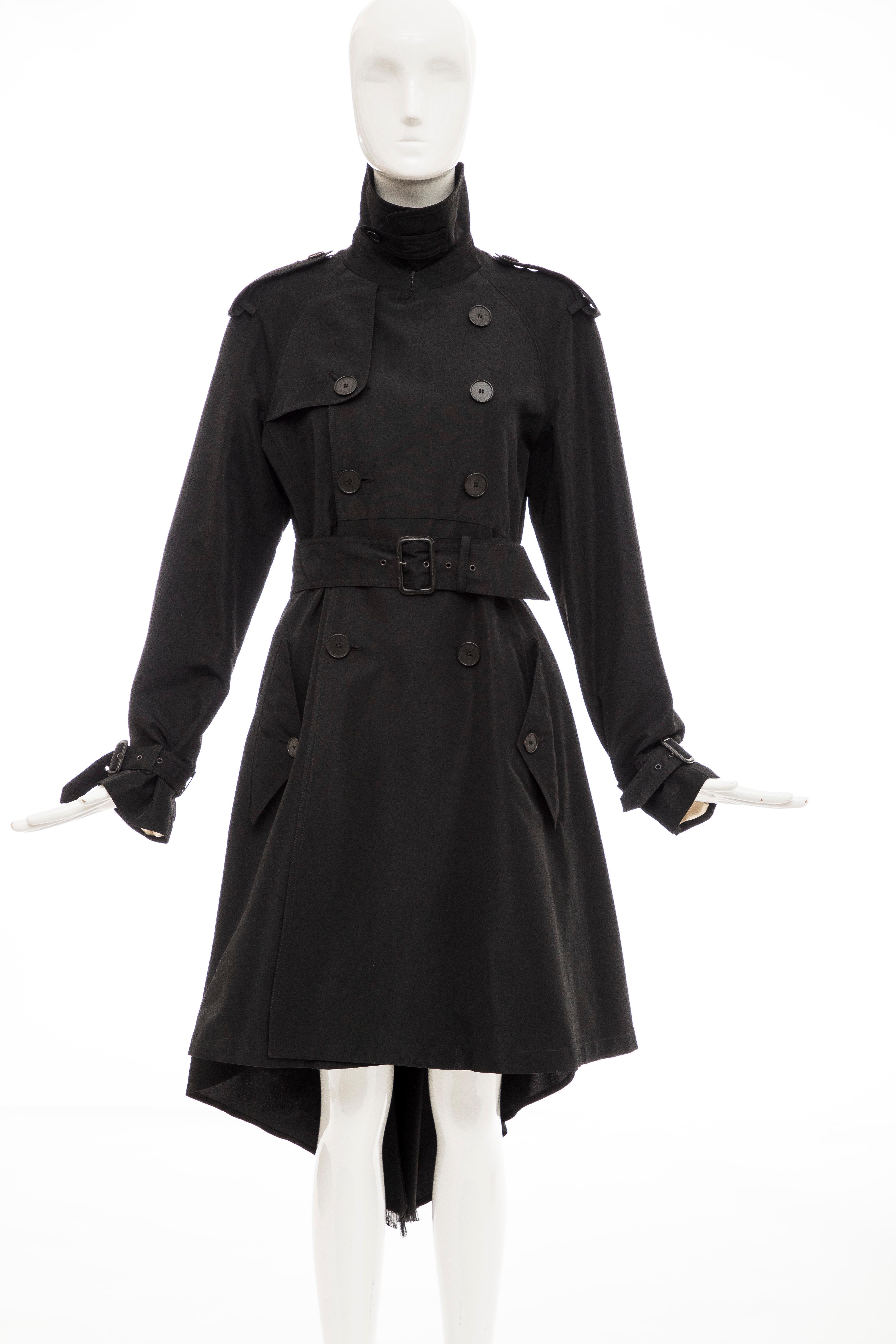  Jean Paul Gaultier, Fall 2007 black double-breasted trench coat with pointed collar, shoulder epaulets, dual flap pockets at sides, adjustable belt at waist featuring bow accent at back, fringe-trimmed high-low hem and button closures at front.