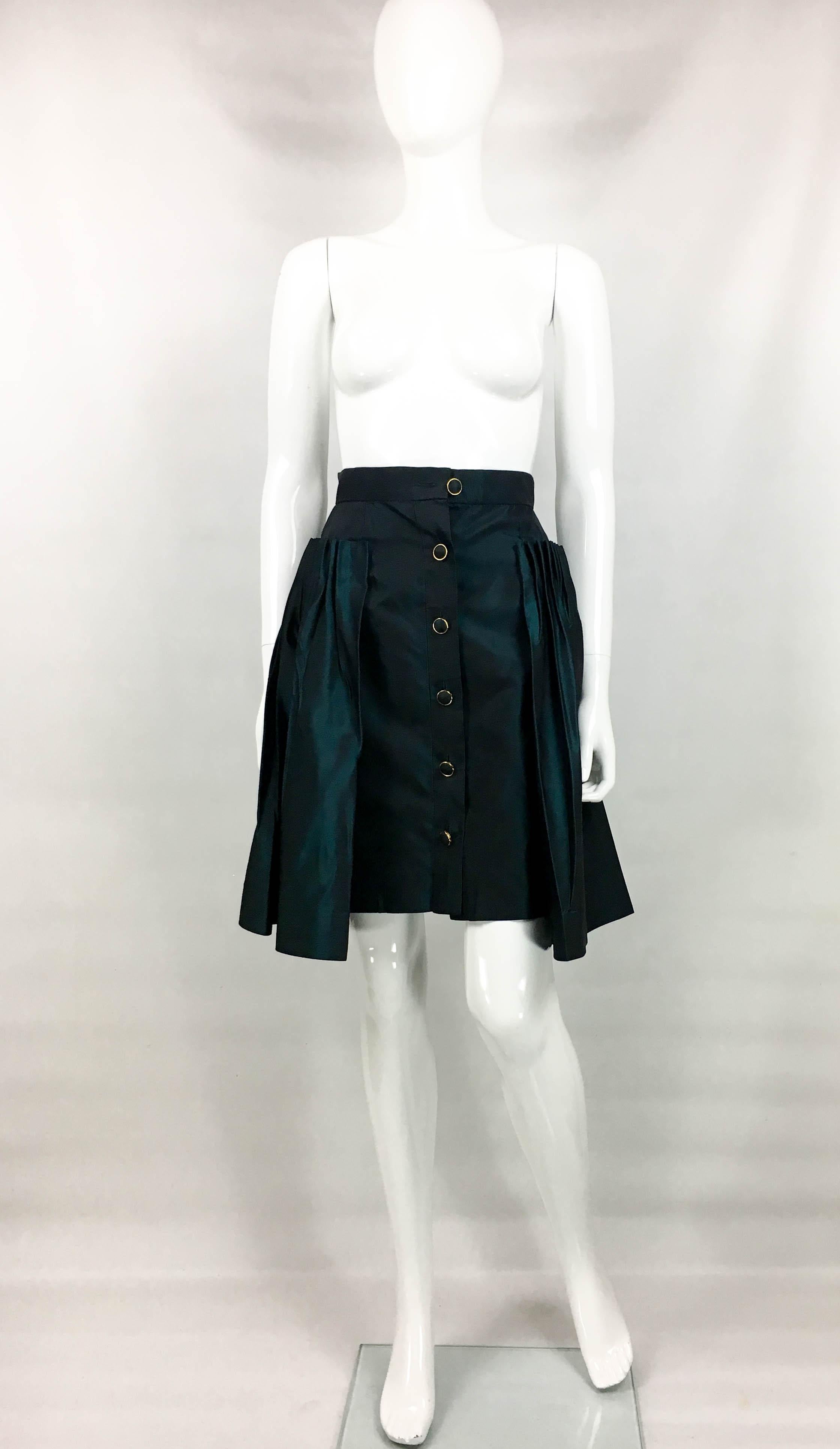 Vintage Chanel Iridescent Green Skirt. This beautiful piece by Chanel dates back from the 1990’s. Made in iridescent green silk, it has pleated volume from the hips. There are six buttons down the front. They are made in gilt metal with the centre