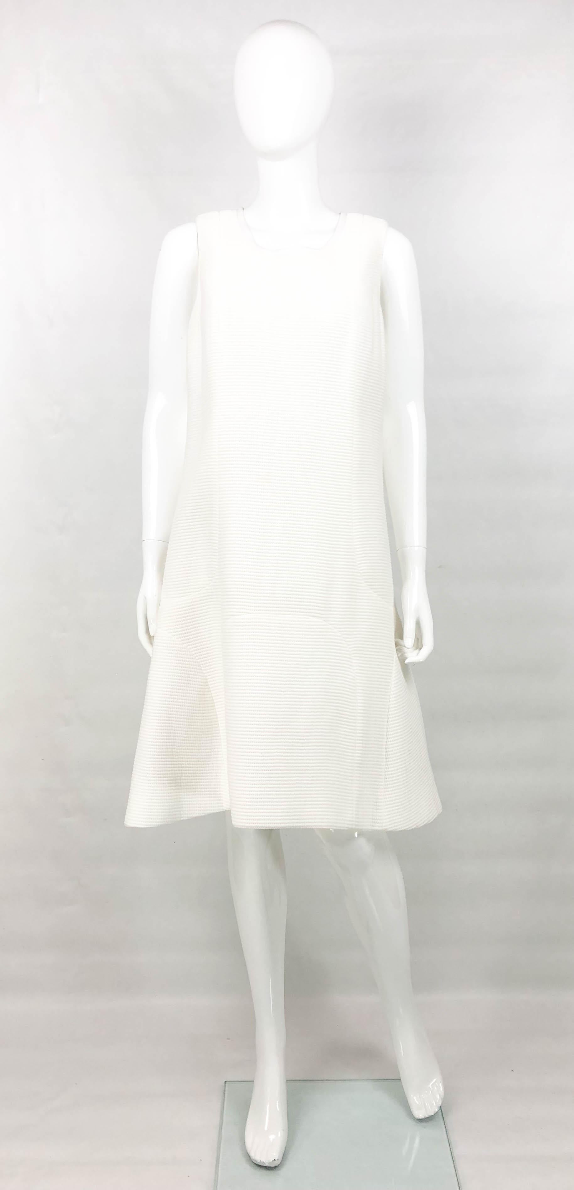 Chanel White Waffle Cotton Dress. Made in waffle textured cotton, this beautiful dress by Chanel is inspired by the 1960’s A-line silhouette. Sleeveless, it is lined in silk. A simple and timeless dress made for the effortless elegant woman. 

Label