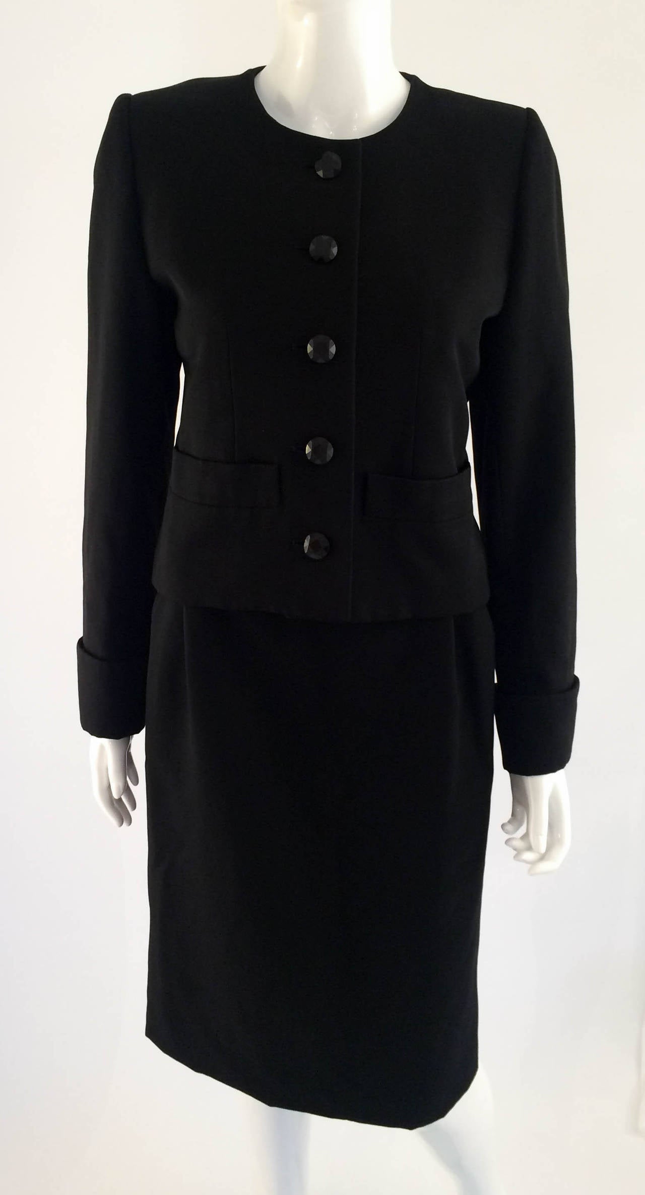 Elegant Vintage Yves Saint Laurent Wool Suit. Straight shaped, below the knees skirt with 2 side pockets. The jacket is single breasted with a jewel neckline and sleeves with rolled up cuffs. Fully lined. The buttons are facetted. This is a very