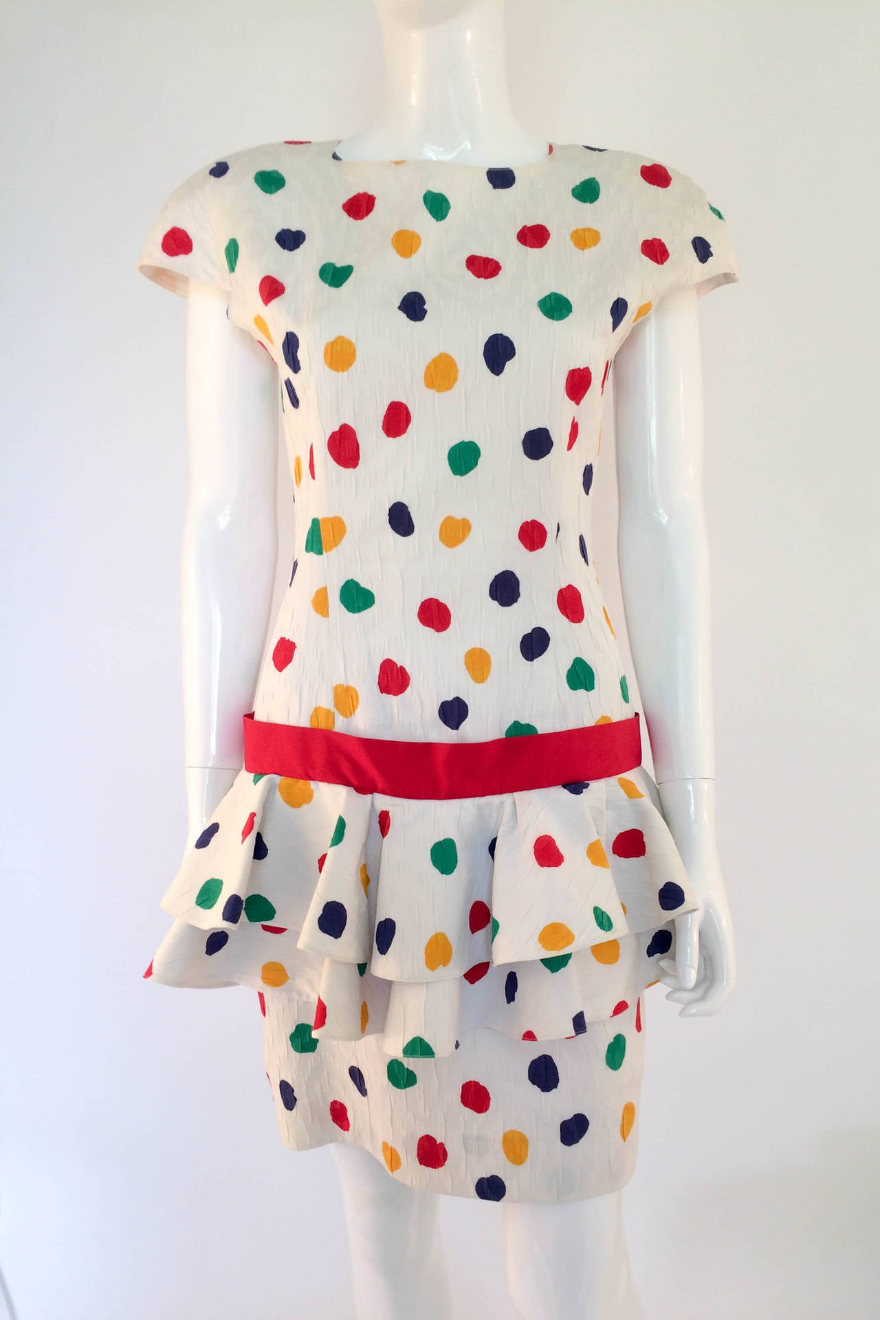 Jazzy rare Guy Laroche cocktail dress. Textured white cotton with red, blue, yellow and green polka dots.  Two tiered layers around the hips, red ribbon belt, triangular cut-out on the back. The sleeves stick out creating a great silhouette. This is