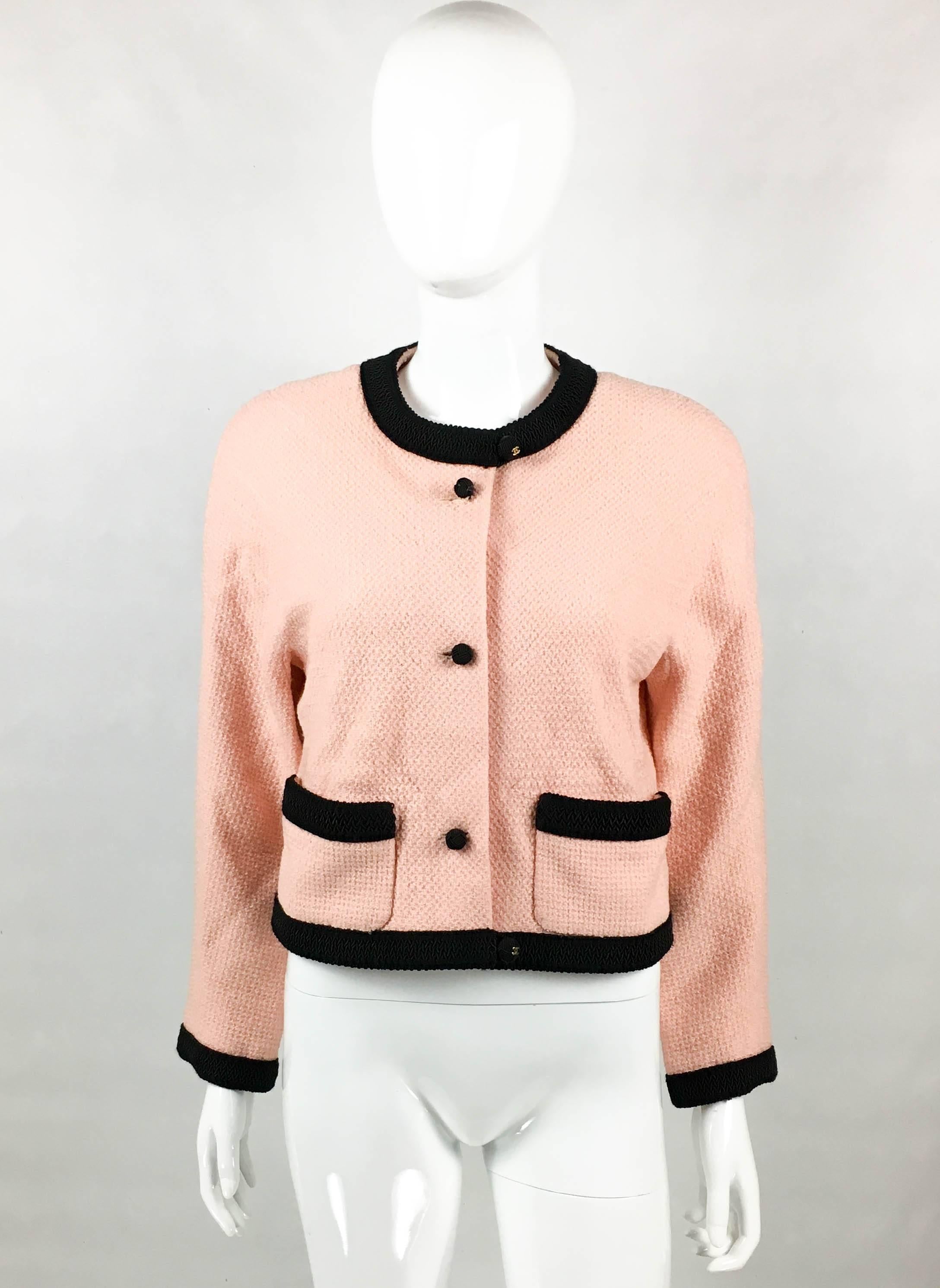 Vintage Chanel Pink Tweed Jacket. This beautiful jacket by Chanel was created in the 1990’s. In pink tweed, it features black knot buttons and black cord trims to the collar, hemline, cuffs and pockets. The buttons on the collar and hemline have a