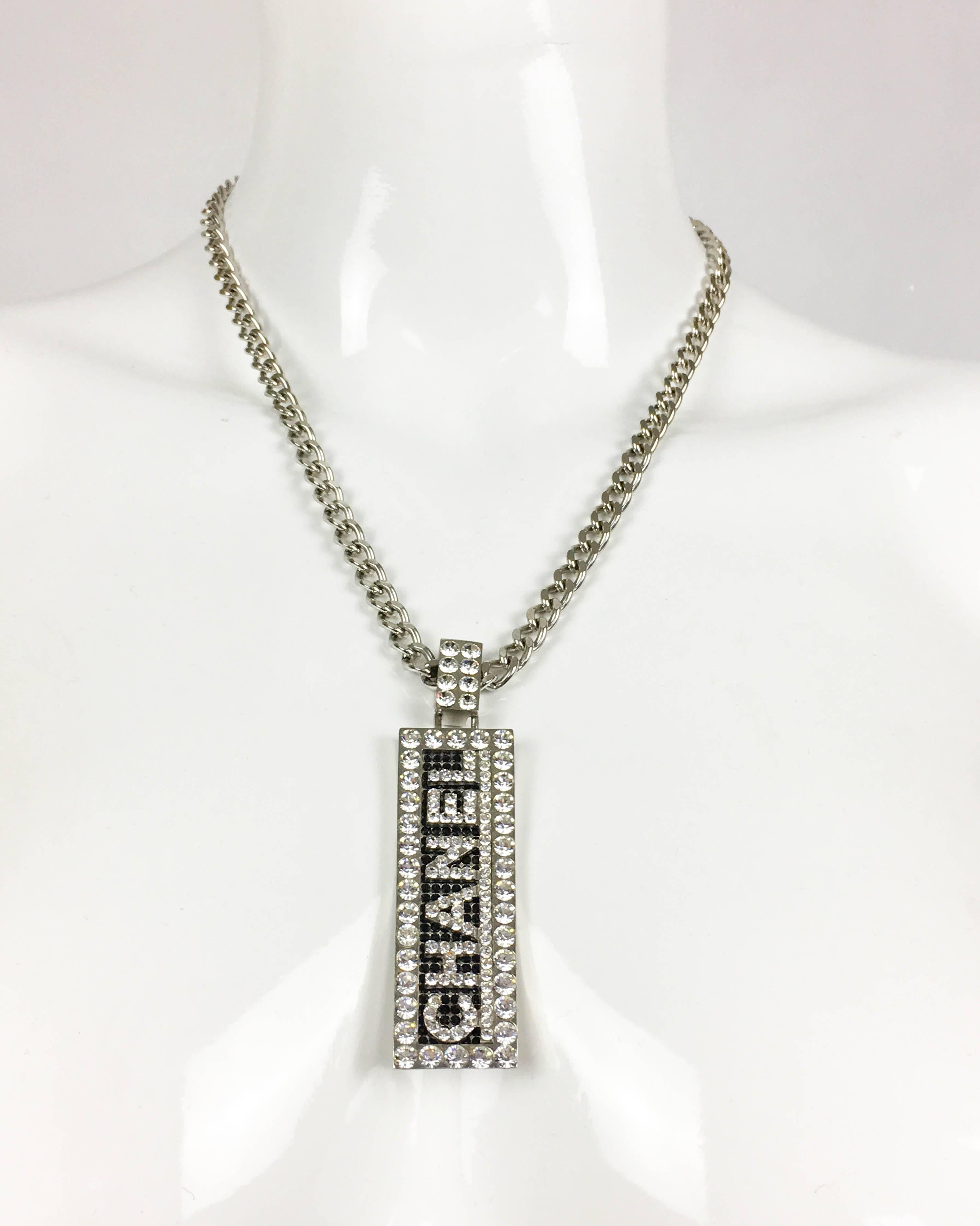 Chanel Rhinestone Plaque Pendant Necklace. This gorgeous piece by Chanel was created for the 2003 Fall / Winter collection. It features a white metal chain with plaque pendant saying Chanel in white crystals on a black rhinestone background. Chanel