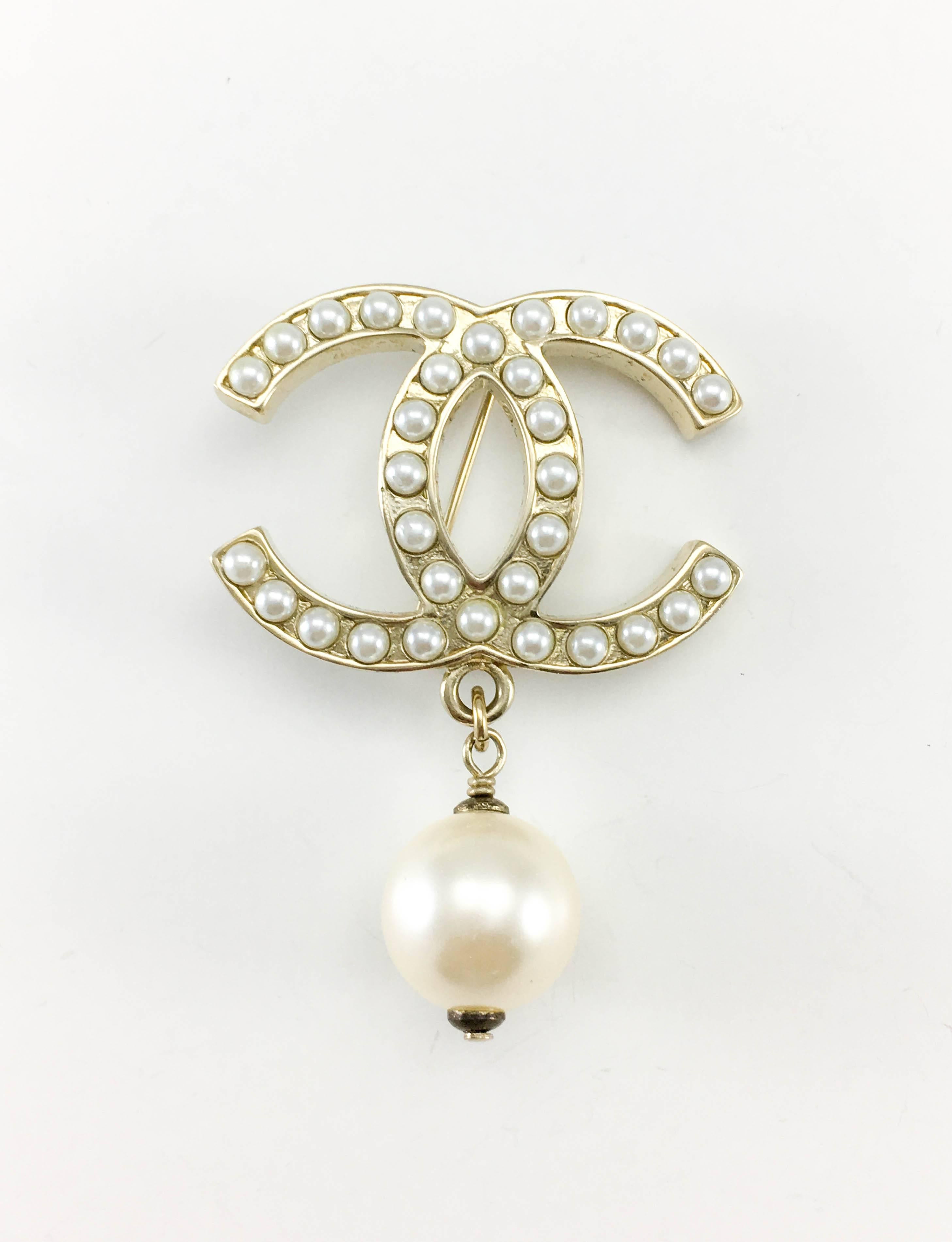 Chanel Pearl Logo Brooch. Dating from 2012, this brooch is quintessentially Chanel. Made in gilt metal, it has the iconic ‘CC’ logo adorned with faux cabochon pearls with a larger faux pearl drop. Chanel signed on the back. An instant dash of