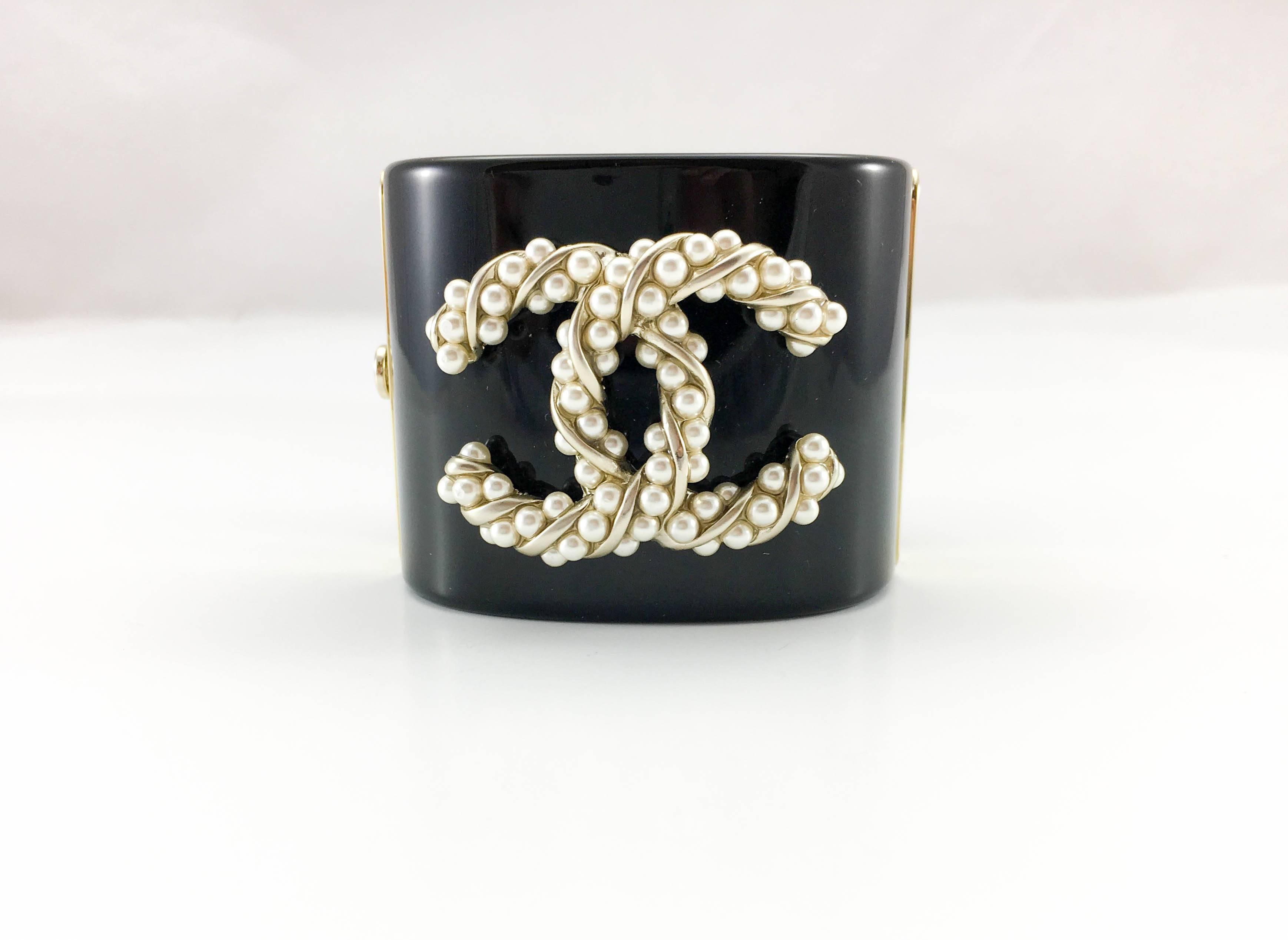 Striking Chanel Pearl Logo Cuff Bracelet. This beautiful piece by Chanel was crafted for the 2015 Autumn / Winter Collection. The black resin cuff is adorned with a large, baroque-style pearl logo, a recurrent theme at Chanel. The closure is by a