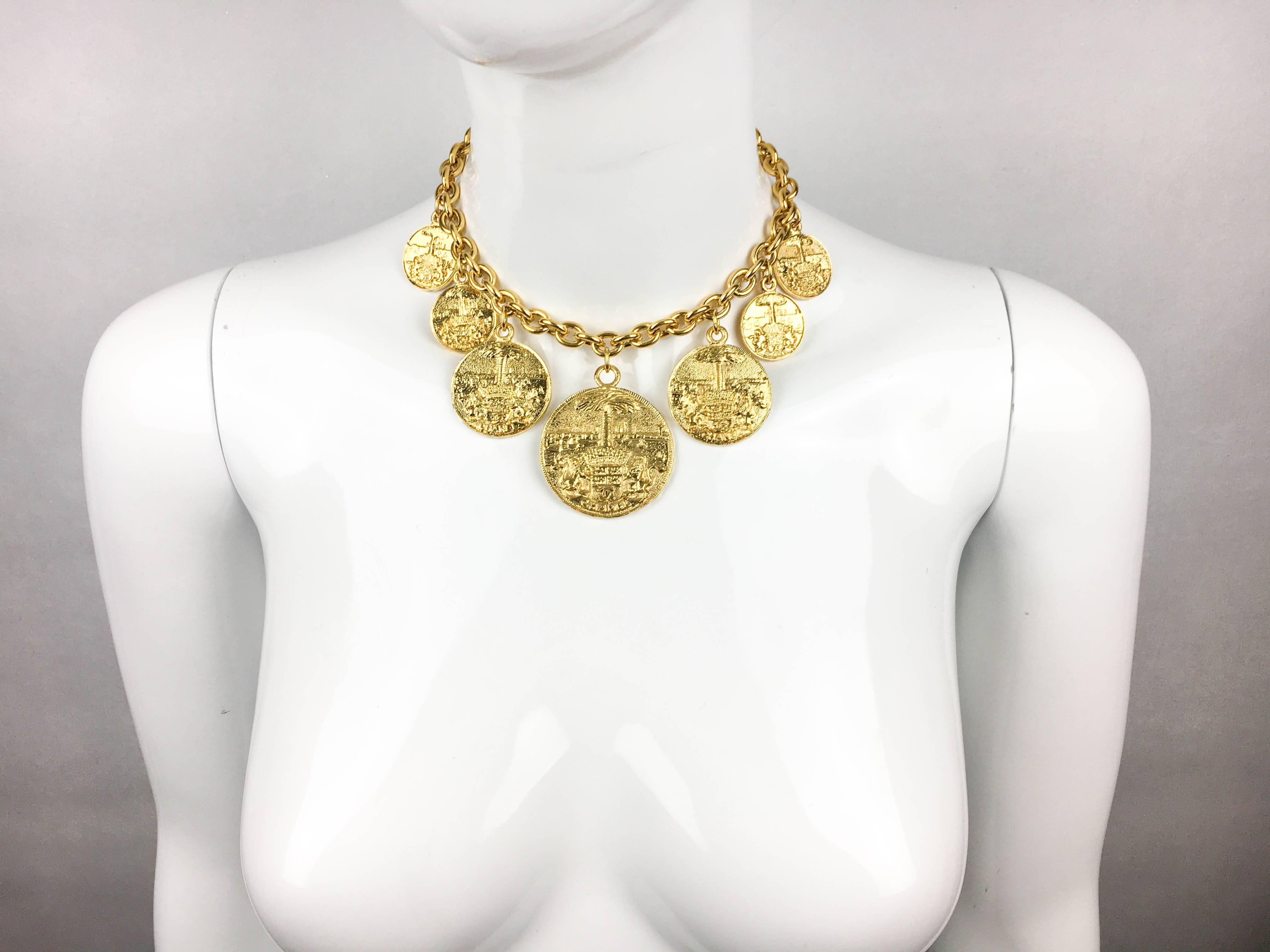 Vintage Chanel Gilt Medallion Choker Necklace. This beautiful Chanel necklace dates back from the 1980’s. It comprises of a chain with 7 medallions hanging from it. They feature a seal and landscape design and are graduated in size, with the largest