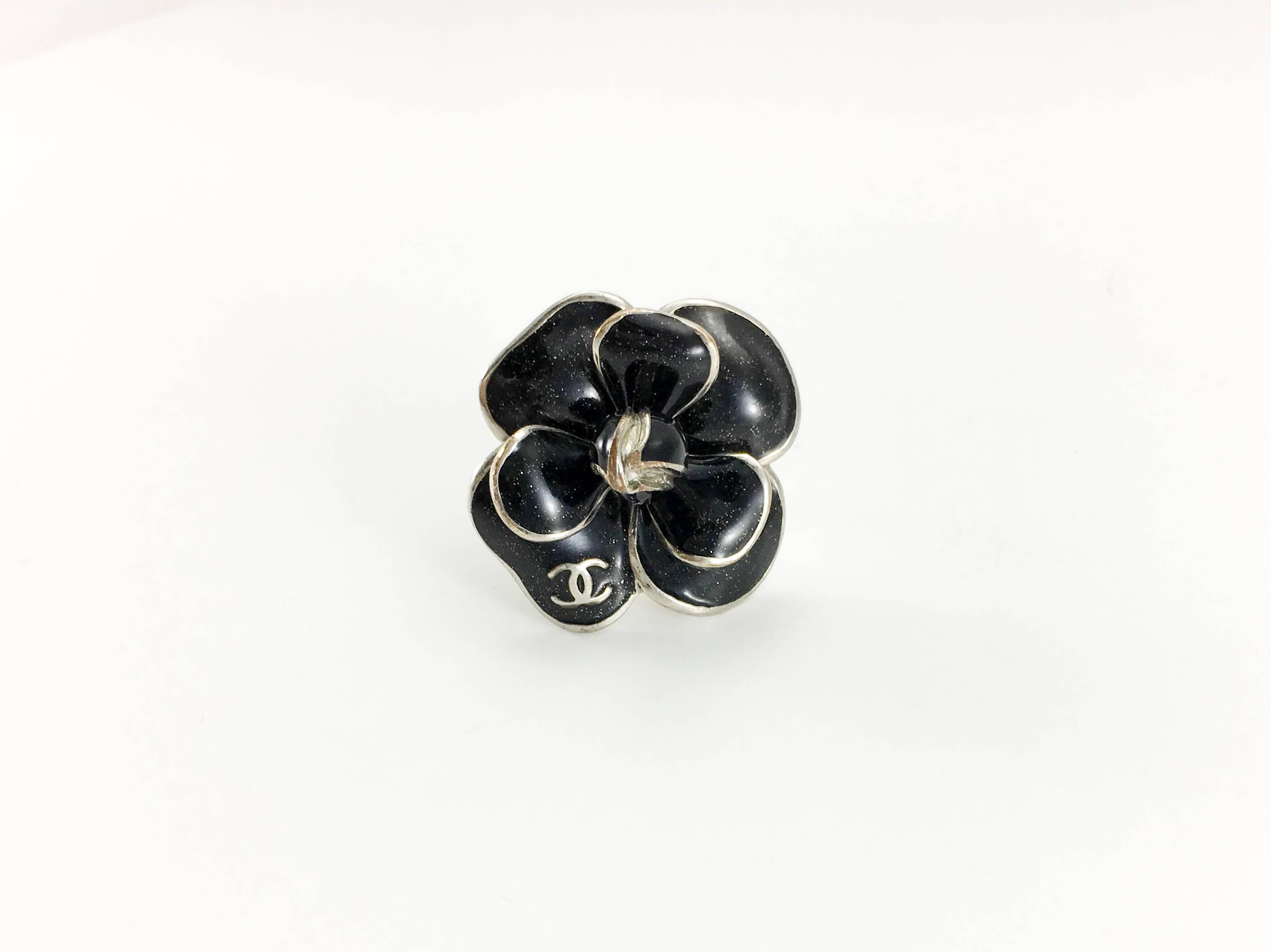 Chanel Black Enamel Camellia Ring. This gorgeous ring by Chanel was crafted for the 2008 Spring / Summer Collection. In silver-toned hardware, it features a large black camellia on top. The petals are done in shimmery black enamel. The flower has