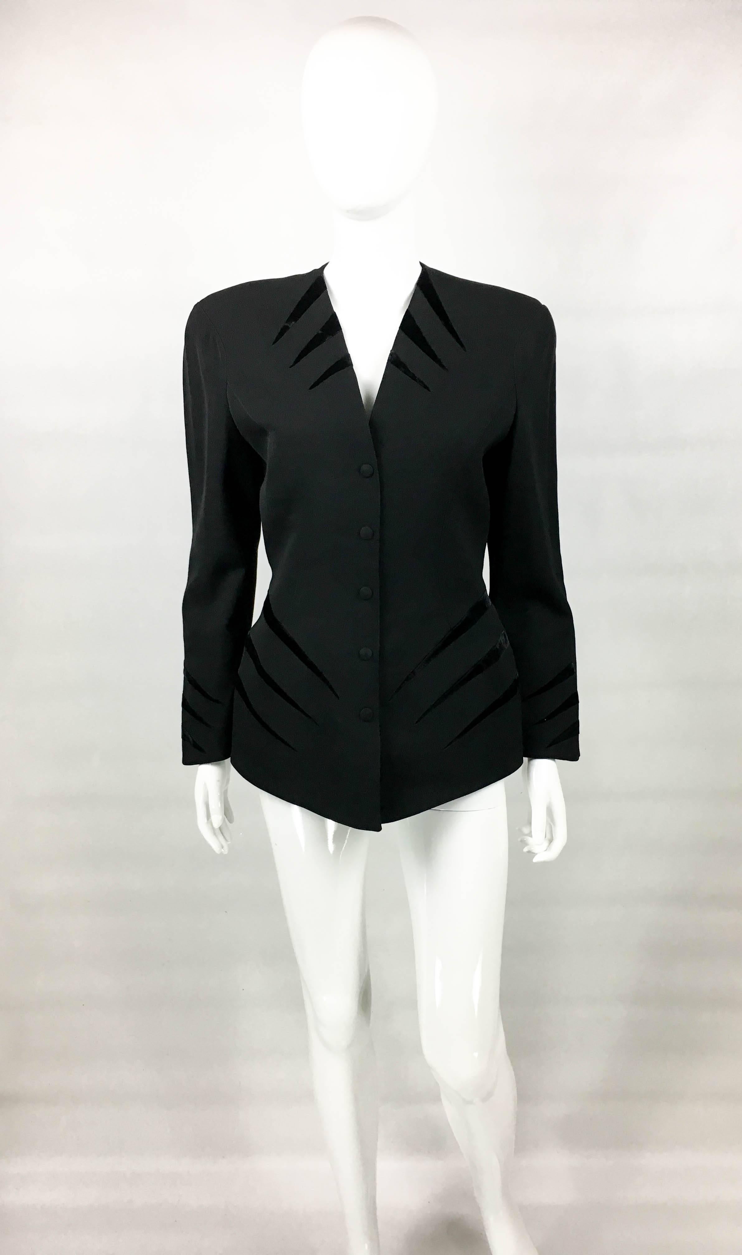 Vintage Mugler Black Wool Jacket. This stylish piece by Mugler dates back from the 1980’s. Made in black wool, it features velvet details on the hips, collar and cuffs. There are 5 covered pressure buttons down the front. The tailoring cinches in