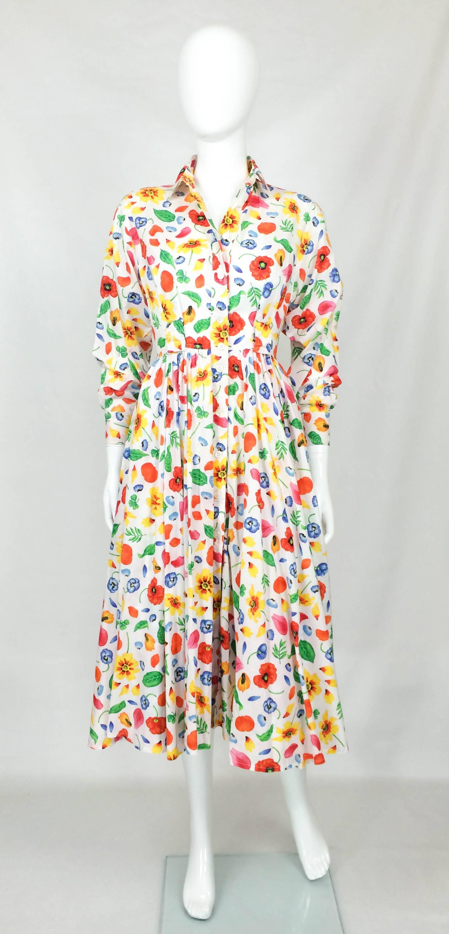 Delightful Floral Print Kenzo Shirt Dress. This is classic use of colours in bold prints by Kenzo. On white background, the flowers look very vibrant. This dress has barrel sleeves, side pockets and is cinched in the waist, giving it a shirtwaist,