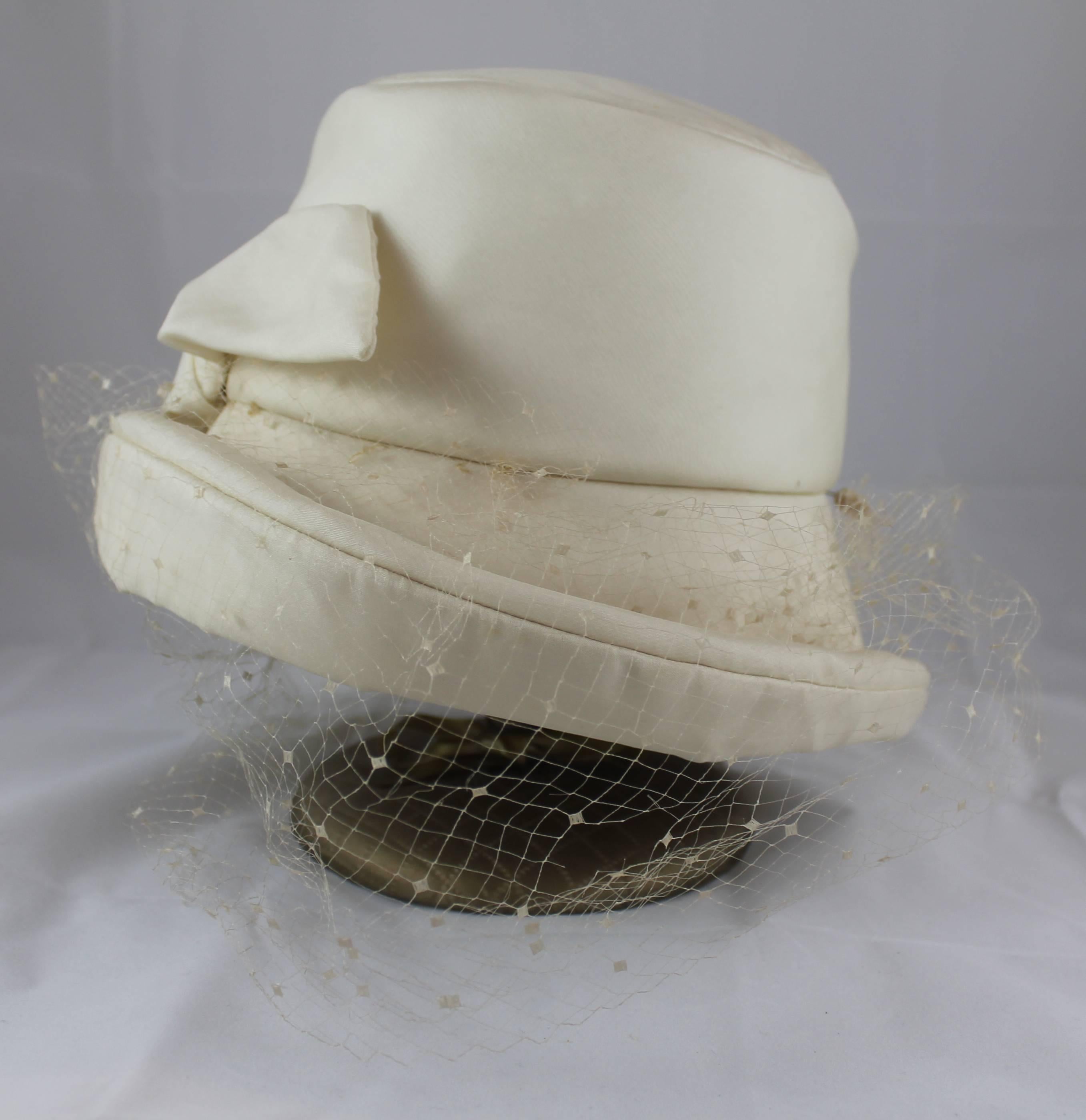 Fleurette Ivory Silk Hat with Bow, Mesh, and Pins. This hat has a front bow and mesh overlay. It has a Gatsby- style feeling to it and the mesh is connected by pins. It is in very good condition with some spots on the top of the inside, a small