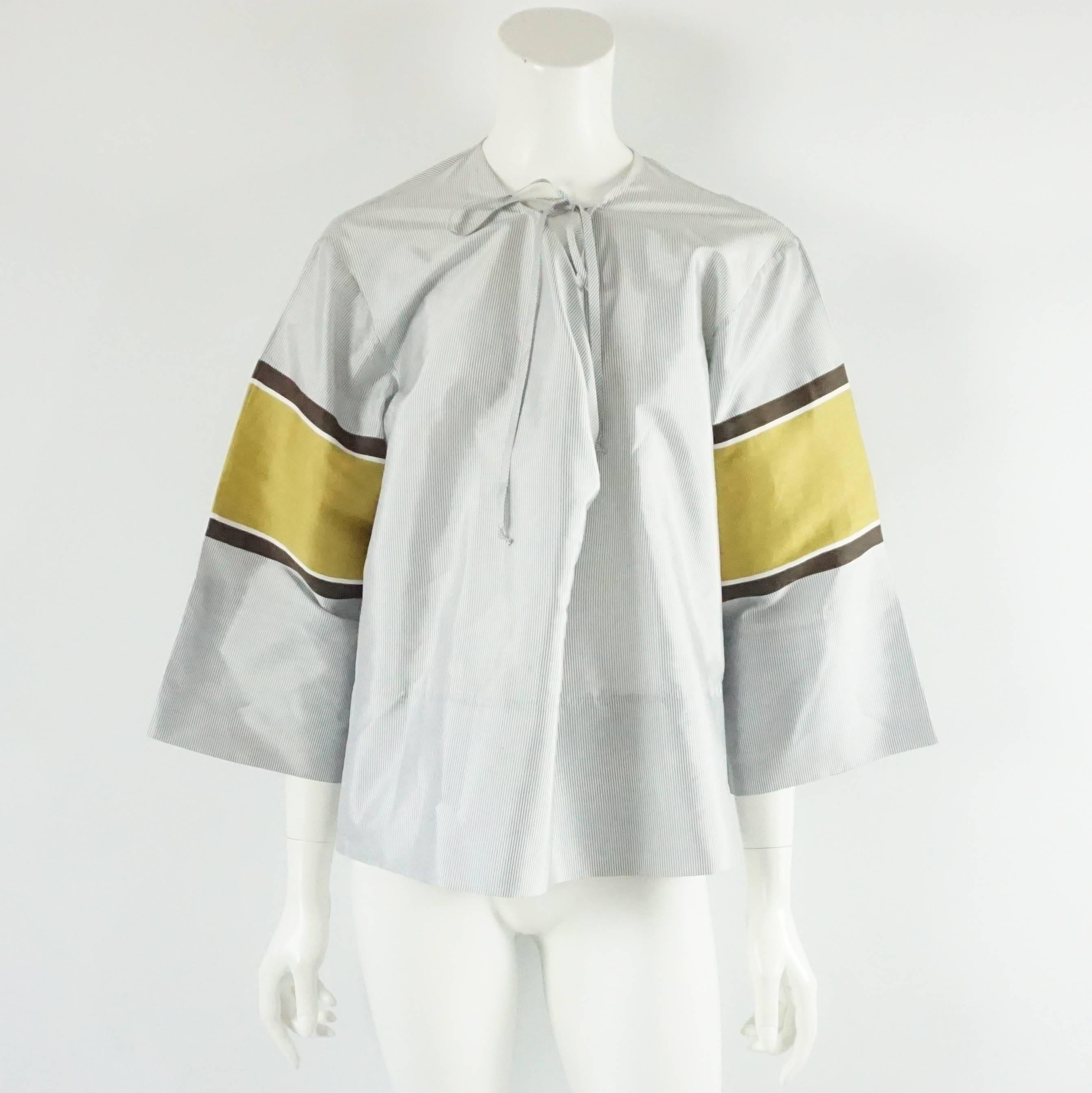 This Bottega Veneta silk top has a loose design. It has blue and white stripes all over and on the sleeves there is mustard and brown detailing. There are ties on the neckline that can be tied to give more structure to the front. This top is in very