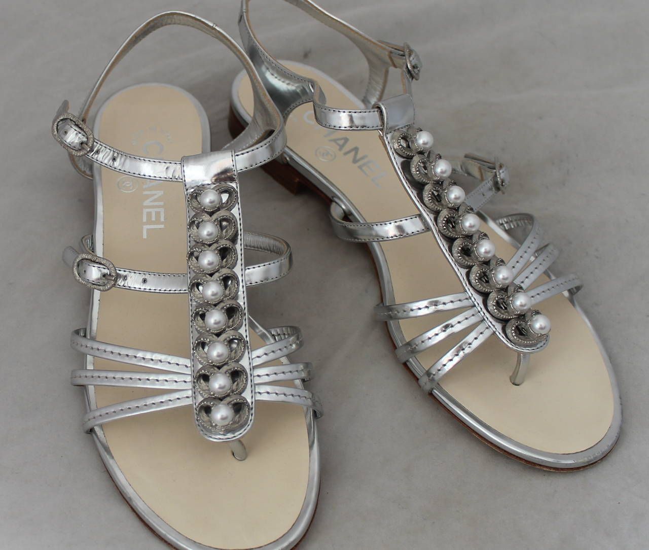 Chanel Silver Metallic Gladiator Sandals with Pearls - 38.5. These shoes are in excellent condition with minor wear on the bottom.