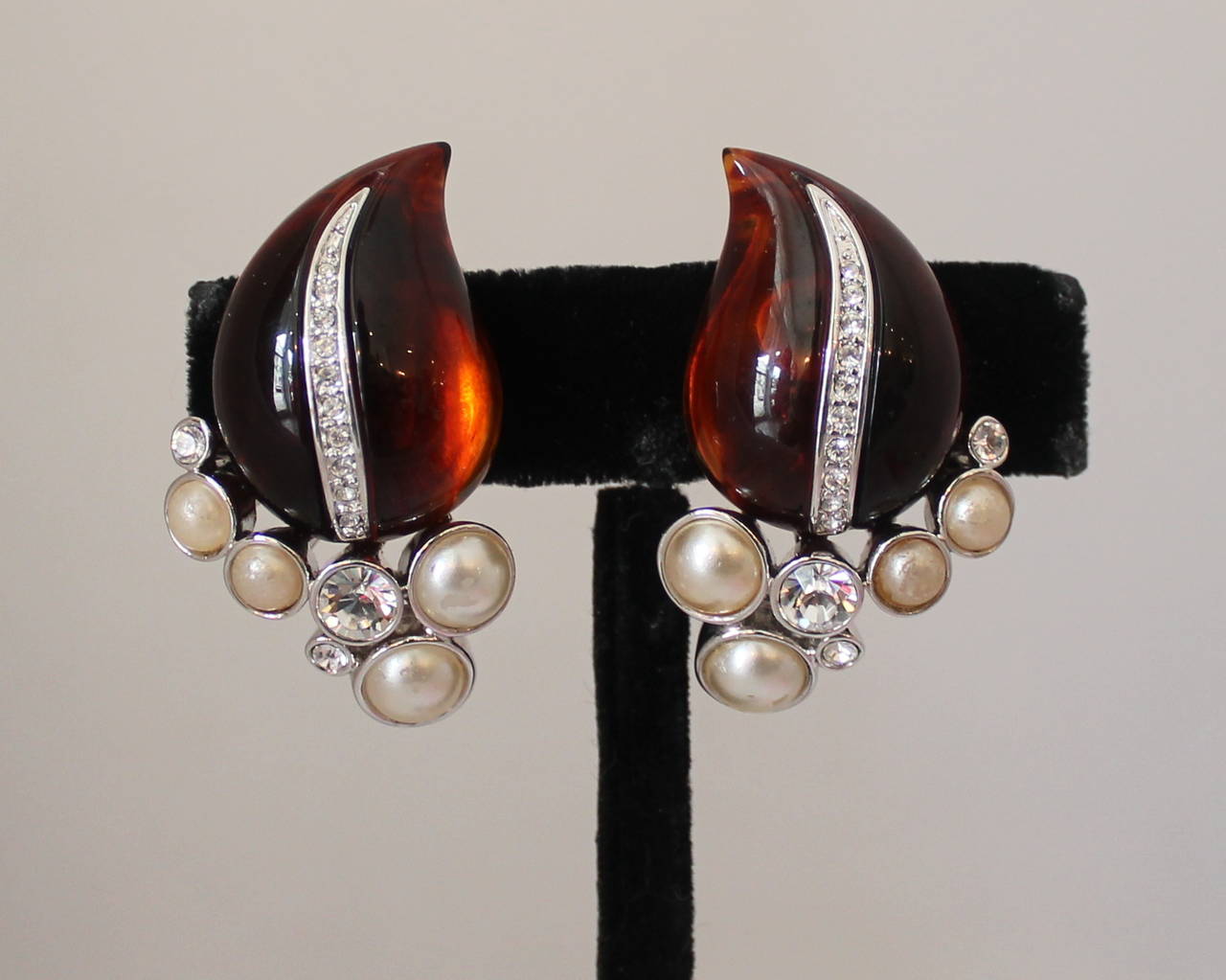 Kenneth Jay Lane 1990's Amber, Leaf & Rhinestone Clip-on Earrings. These earrings are in excellent vintage condition and are a silver-tone. The stone is amber-colored and is adorned with clear rhinestones and pearls on the bottom.

Length-