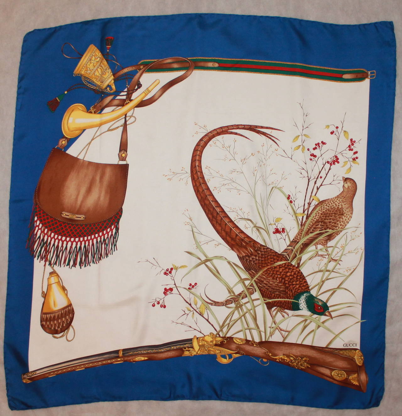Gucci Hunting Large Printed Silk Scarf with Royal Blue Trim. This scarf is in excellent condition and has birds, a horn, and satchel on the print. 

Length- 34