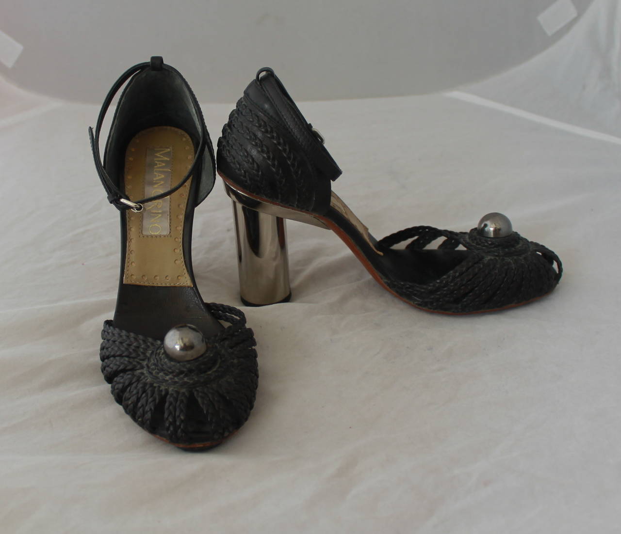 Malandrino 1990's Vintage Black Braided Leather Heels with Ankle Strap -  36.5. These shoes are in good vintage condition with some signs of age by dulling on the leather. The shoe has a thick silver heel and a thin ankle strap. It has some wear on