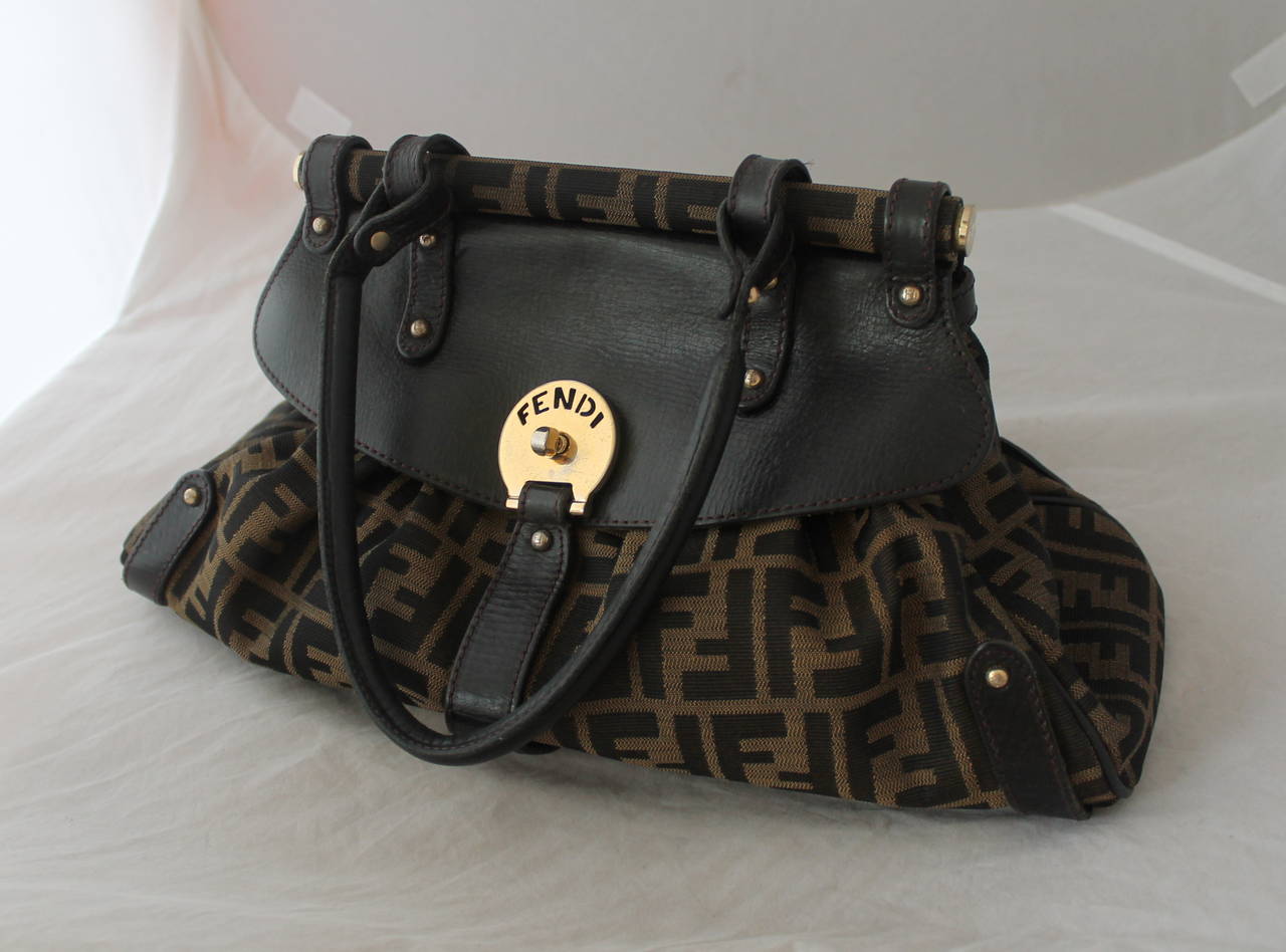 Fendi Brown Monogram Print & Leather Top Handle Shoulder Bag. This bag is in fair condition with wear and some discoloring on the hardware (image 5), wear on the leather, and wear & a stain on the inside (image 7).

Height- 10