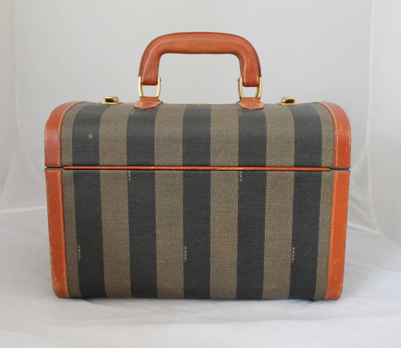 Fendi 1980's Vintage Olive & Black Striped Small Trunk with Brown Leather. It is in fair vintage condition with visible wear. It has 2 gold closures and a numeric lock. There is scuffing all along the leather trim, one visible marking on the handle,