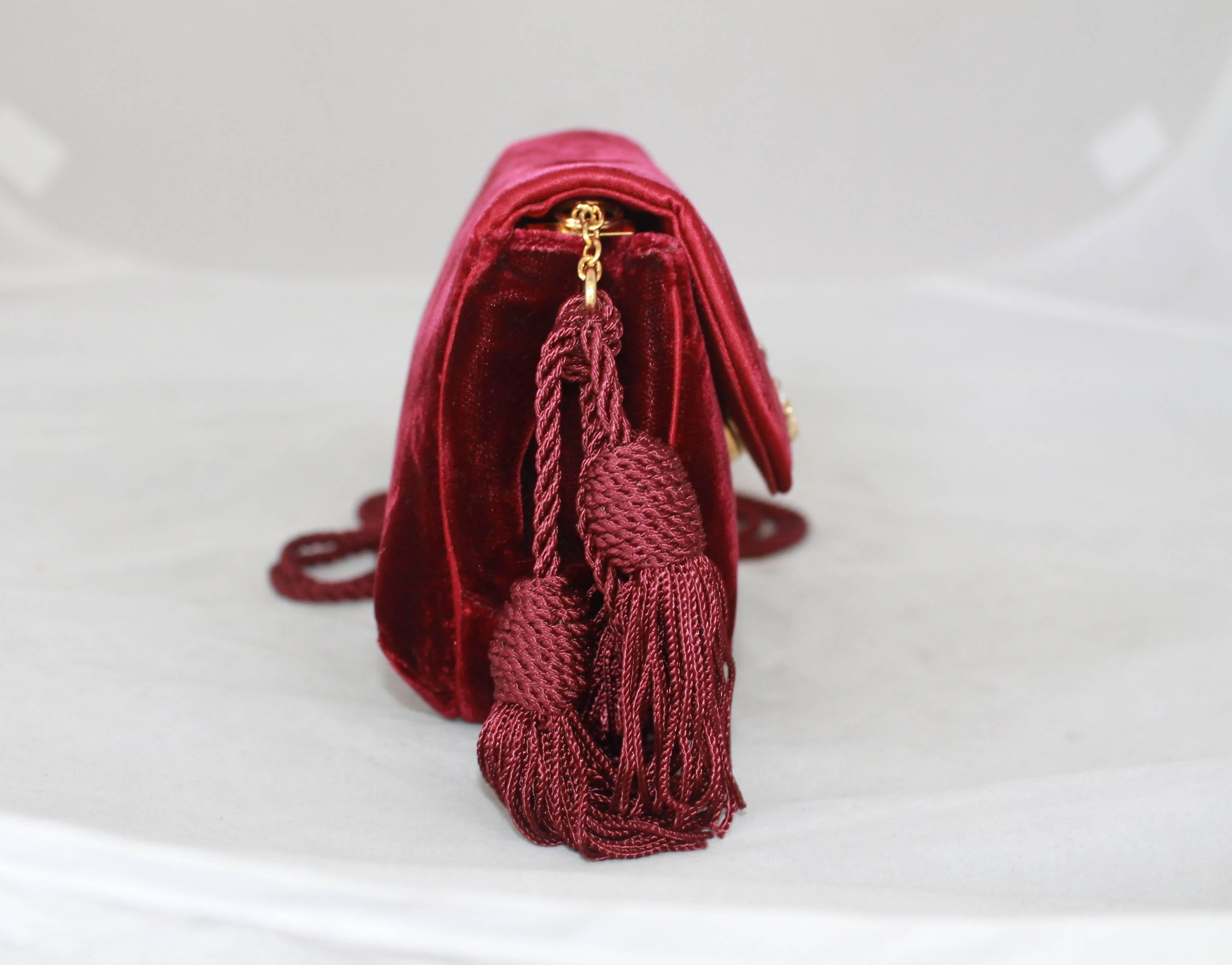 1990's Judith Leiber Vintage Burgundy Velvet Small Evening Bag. This beautiful bag features a double pope long strap and a tassel.  It has a gold medallion with white and red rhinestones.  It comes with a duster.  It is in excellent