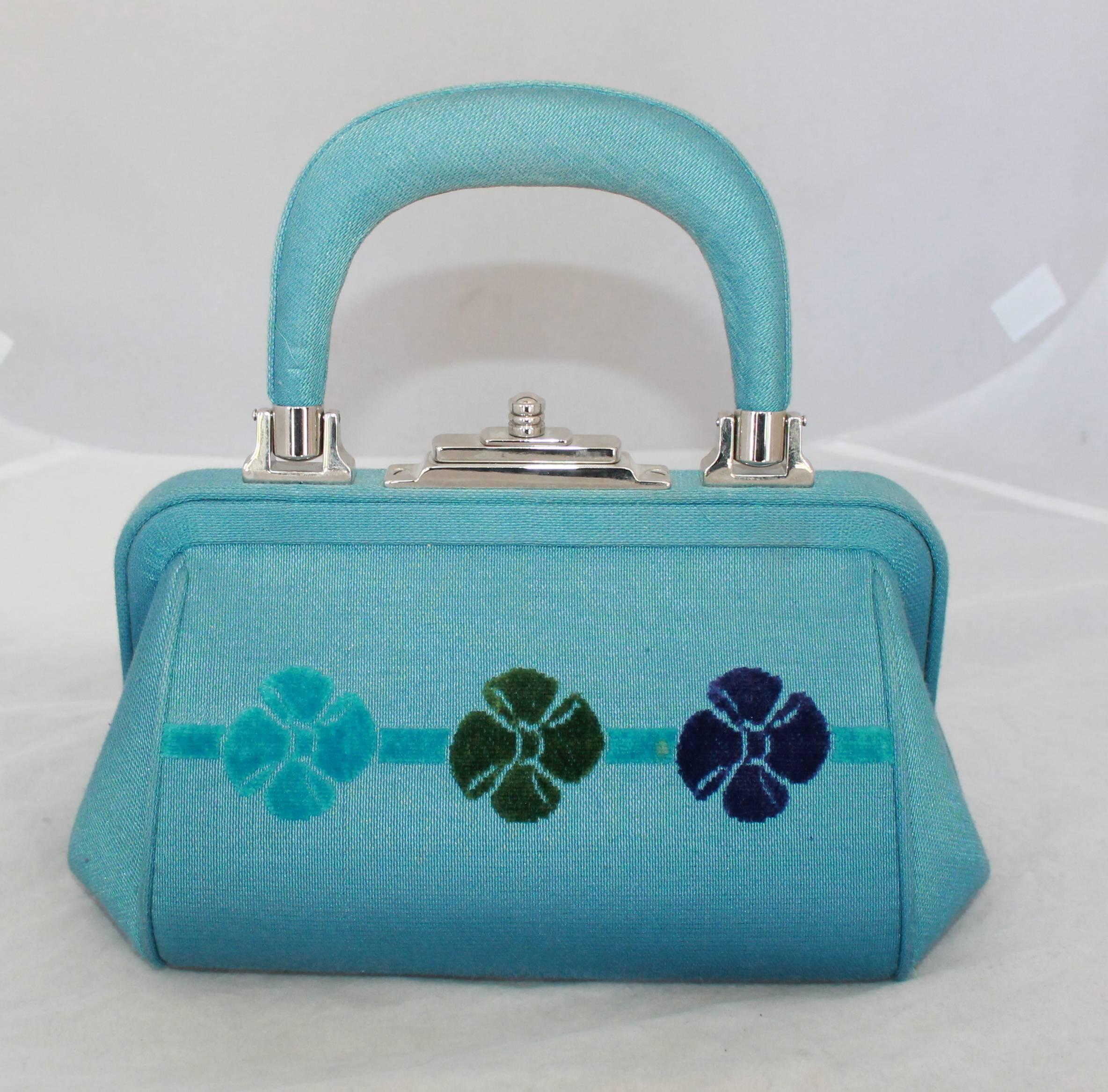 Roberta di Camerino Small Blue Fabric Bag with Flower Design

This bag is in good vintage condition with a small stain on the front left and back right of bag, it also has some wear on handle. It has silver hardware and a top handle with a cut out