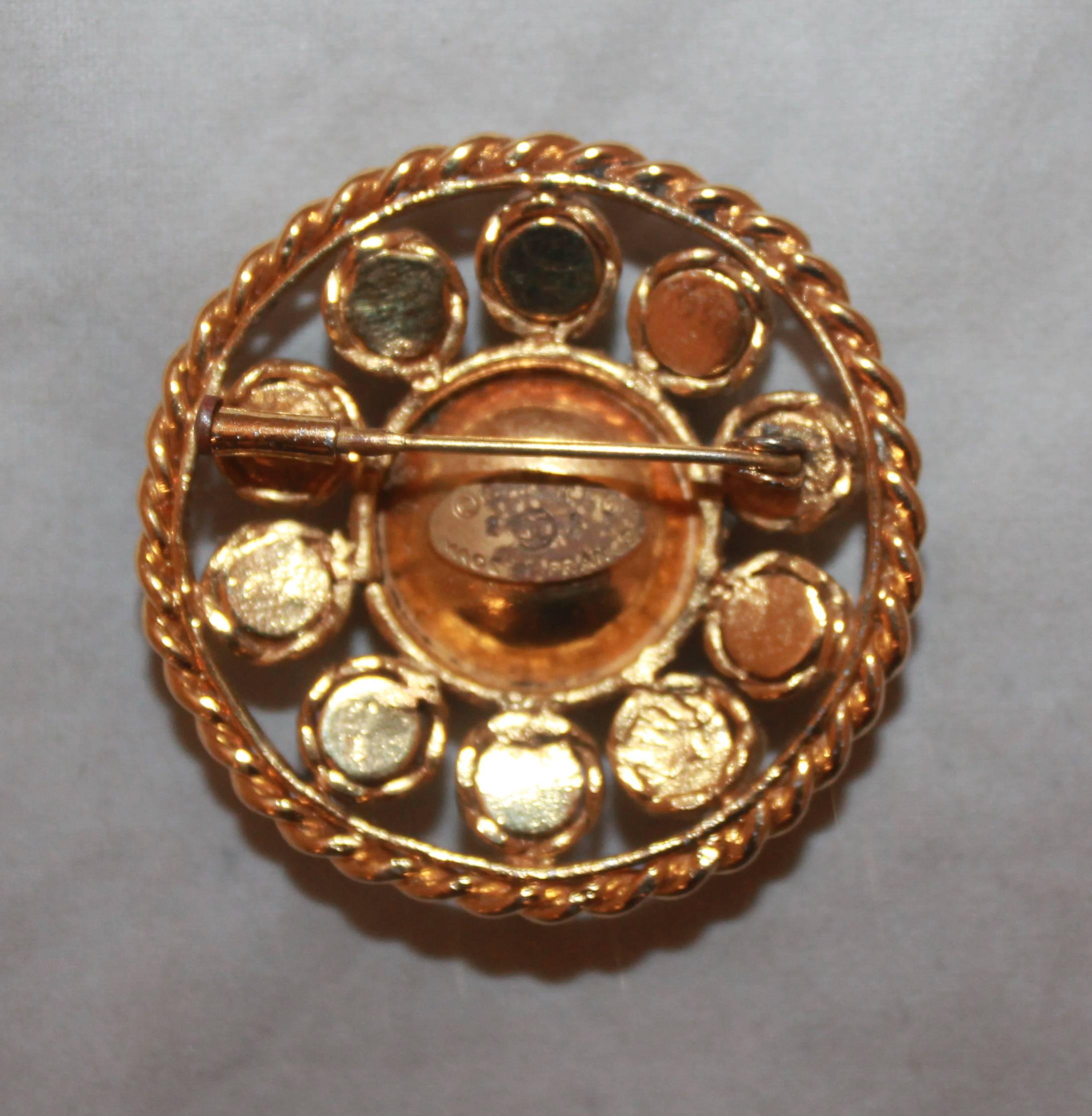 Chanel 1986 Vintage Goldtone Brooch with Blue Gripoix & Rhinestones. This round brooch is in excellent vintage condition and has a braided look on the edge with a cluster of rhinestones and a larger blue gripoix stone in the middle. 

Length &