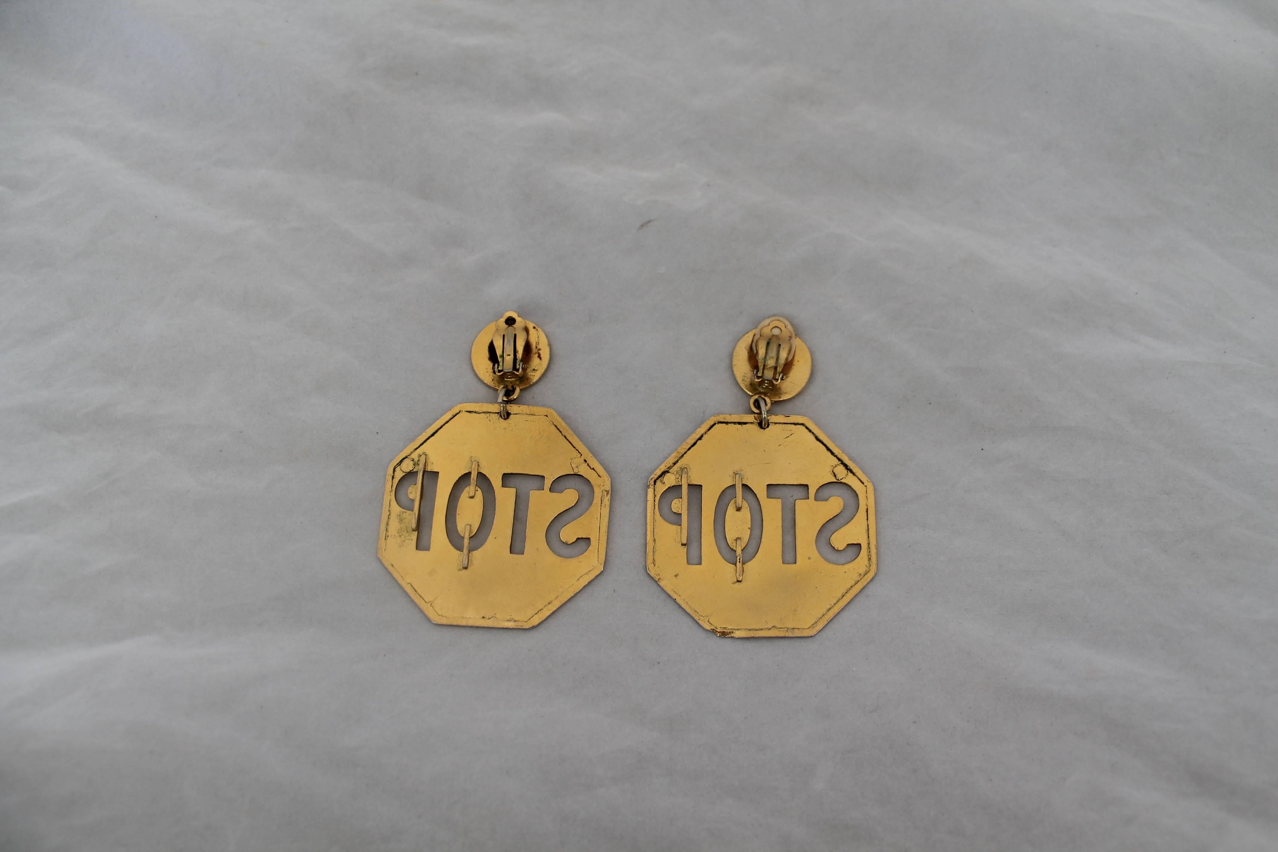 Moschino Vintage Goldtone Stop Sign Clip-on Earrings - circa 1980's. These earrings are in good vintage condition with wear on its color consistent with its age. The backs of one of these earrings has a brown coating on it. 

Length- 3.65