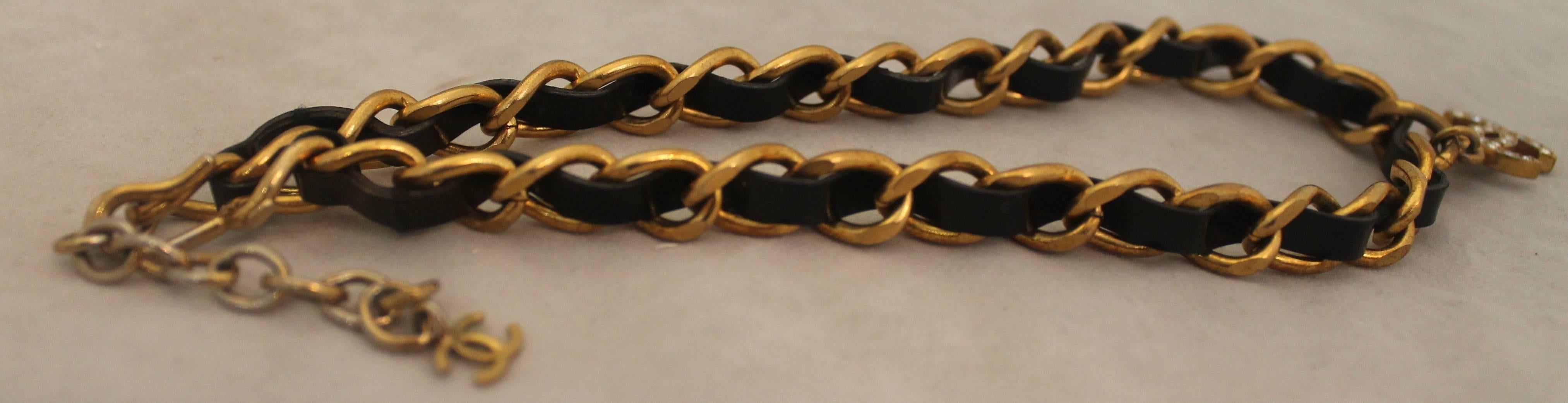 Chanel Goldtone Chain Choker w/ Black Leather and CC Rhinestone - circa 1998. This piece is in very good condition with the chain in the back (where the hook is) being slightly discolored. The leather is a black patent and the 