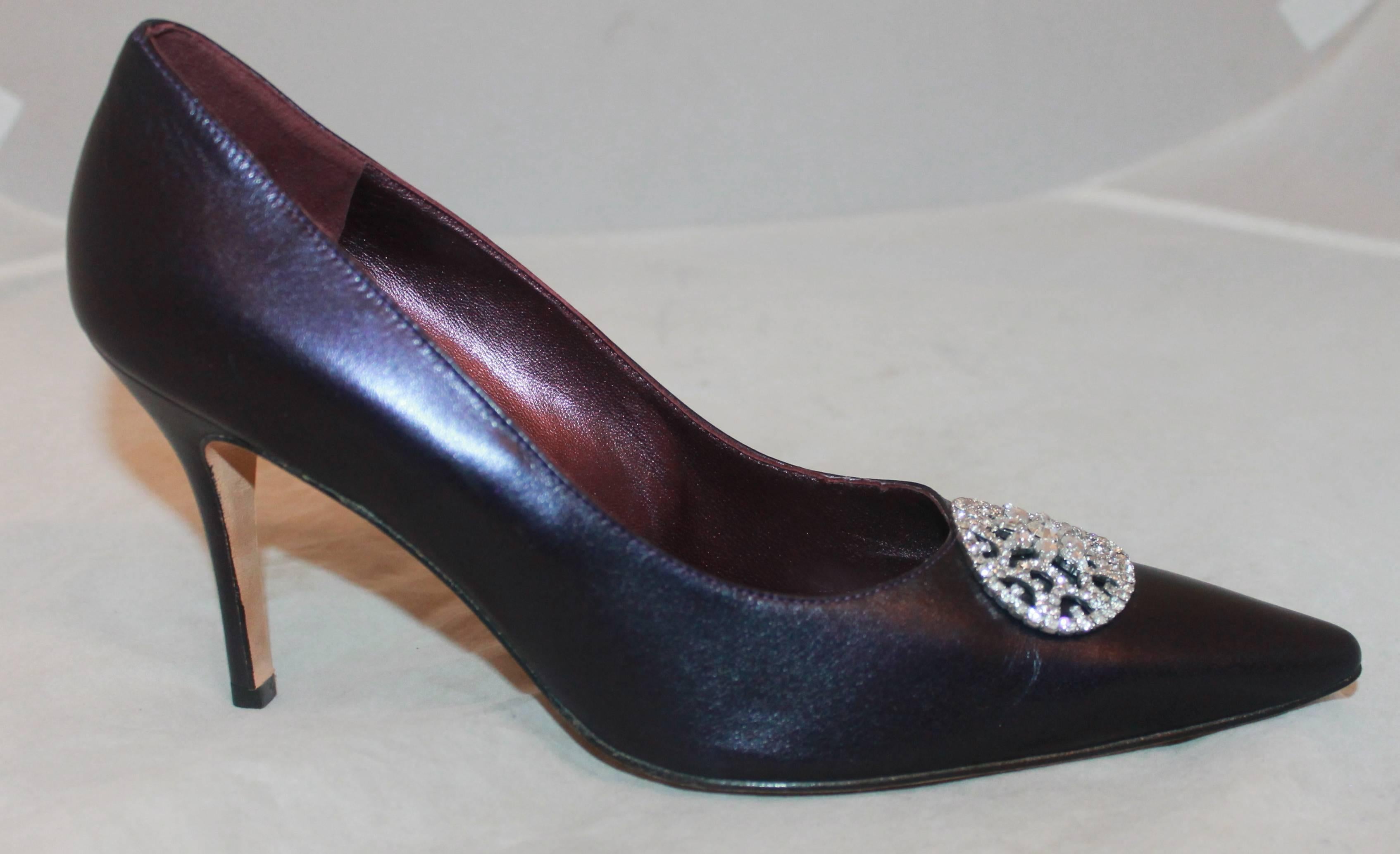 Manolo Blahnik Metallic Eggplant Leather Pumps w/ Rhinestone Pendant - 40.5 - New.  These lovely Blahnik pumps are in new condition having never been worn.  They feature a unique metallic eggplant leather, a rhinestone emblem, and a pointed