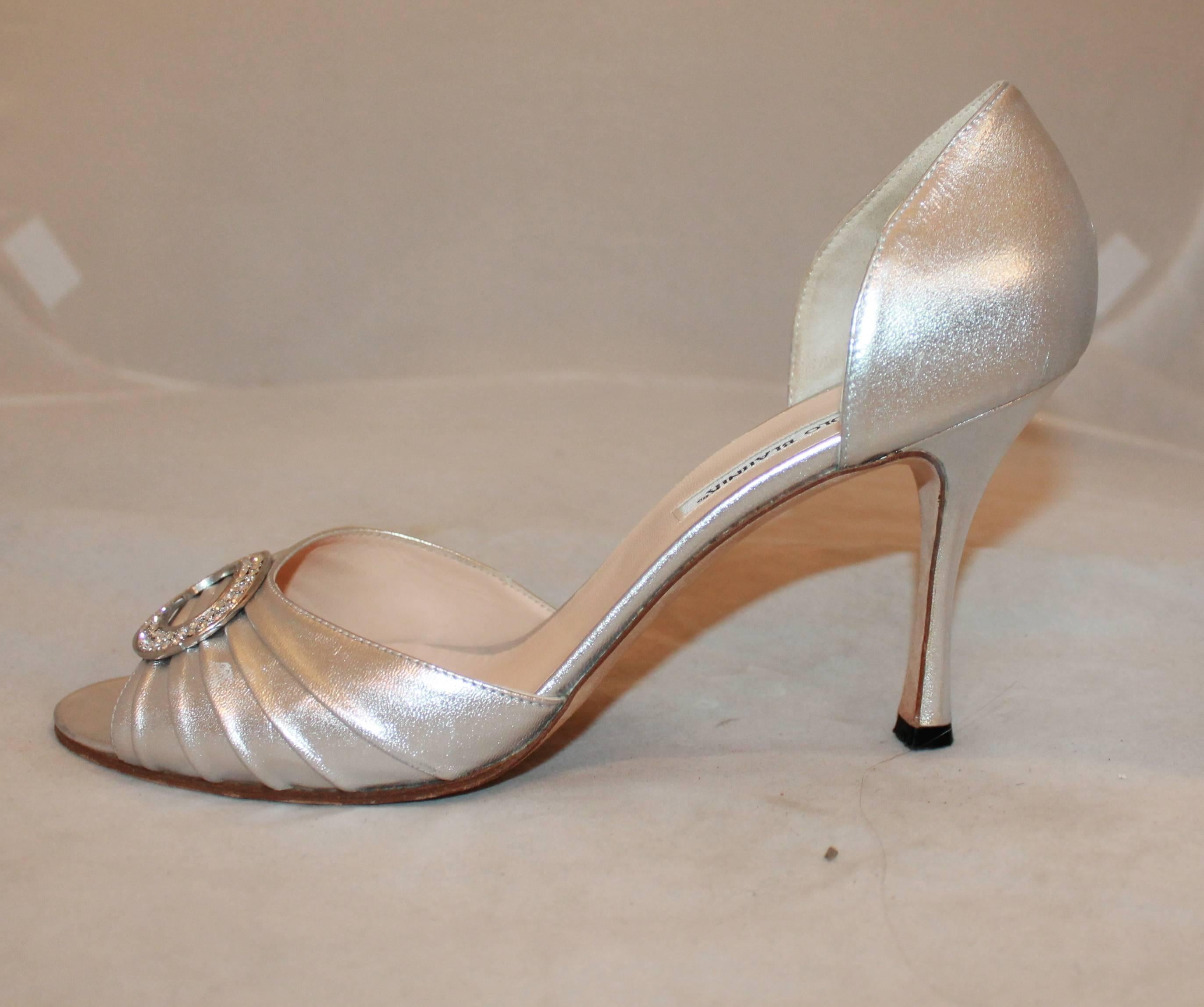 Manolo Blahnik Metallic Silver Leather Heels with Rhinestone Buckle - 41.5. These open-toe heels are a metallic silver and have cinching. They also have a rhinestone-encrusted buckle on the front. They are in good condition and show some scuffs on