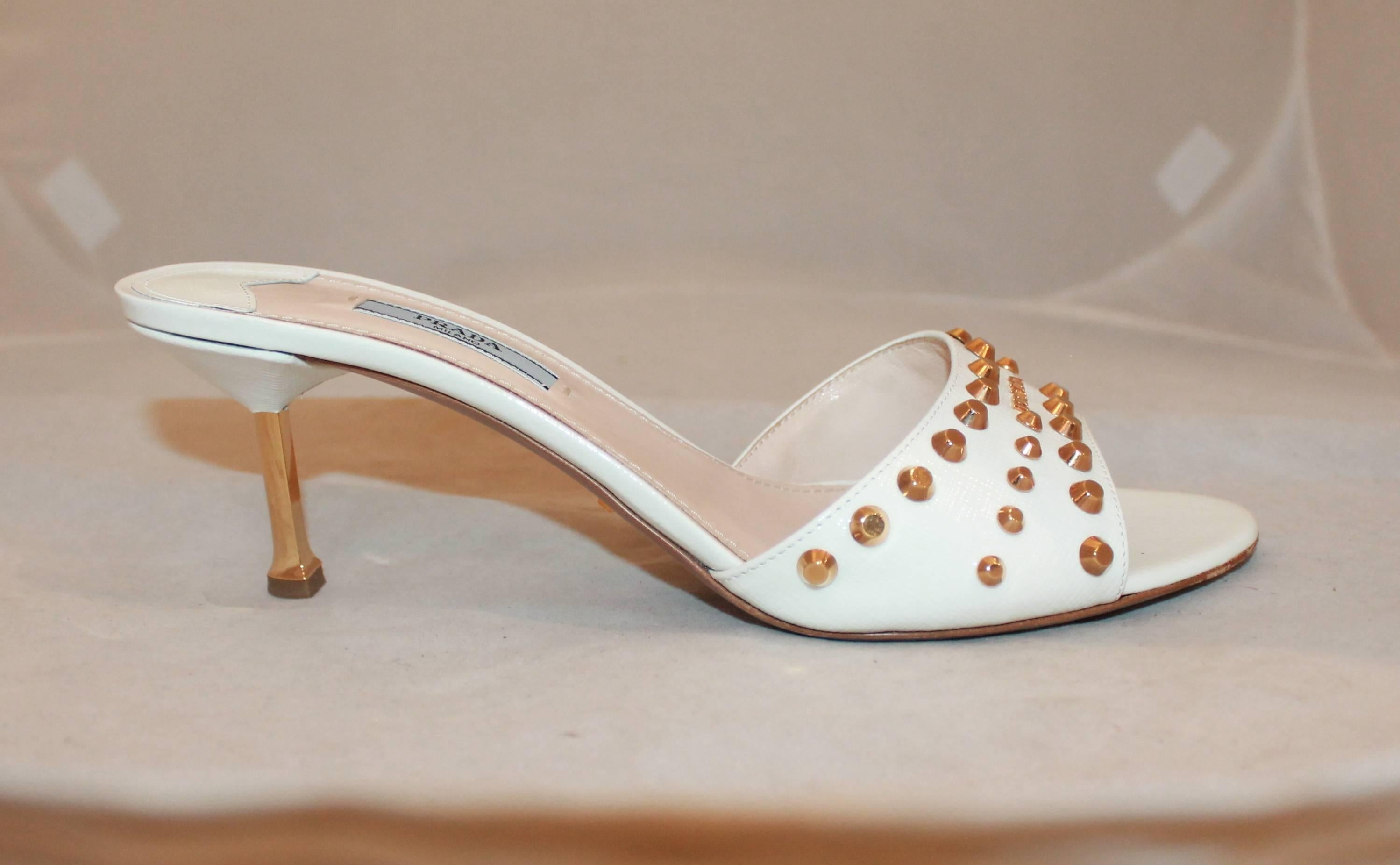 Prada White Saffiano Slides with Gold Heels, Gold Studs and Logo - 39.5. These white, Saffiano leather, Prada slides have a gold heel, gold studs, and a gold logo. They are have some wear on the bottom but are in excellent condition.