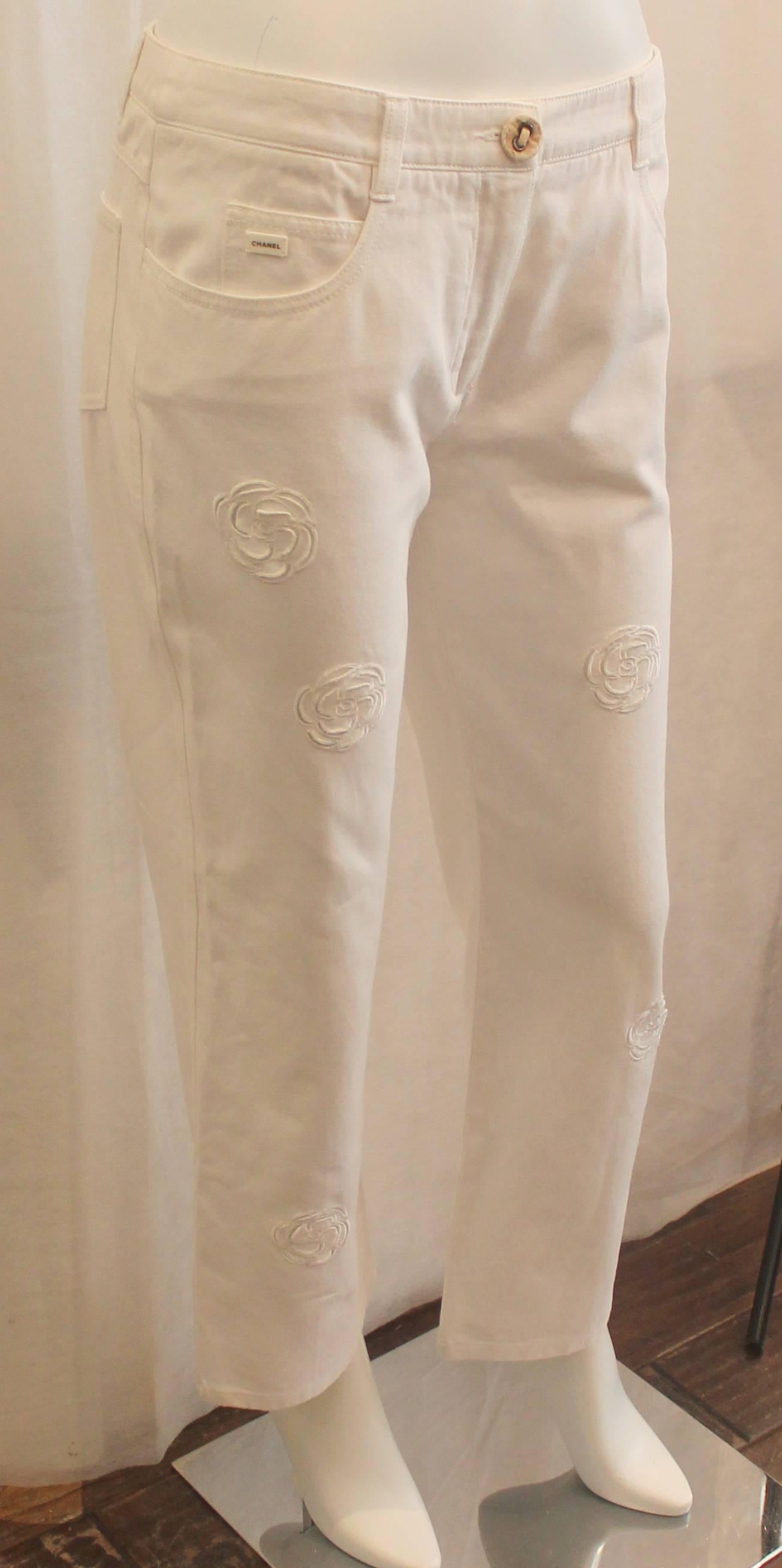 Chanel White Denim Boot Cut Jeans with Camellia Cutouts - 40. These jeans are in good condition with general wear to the fabric. The pants have a beige colored denim button and an enamel mini Chanel plaque on them.

Measurements:
Waist-
