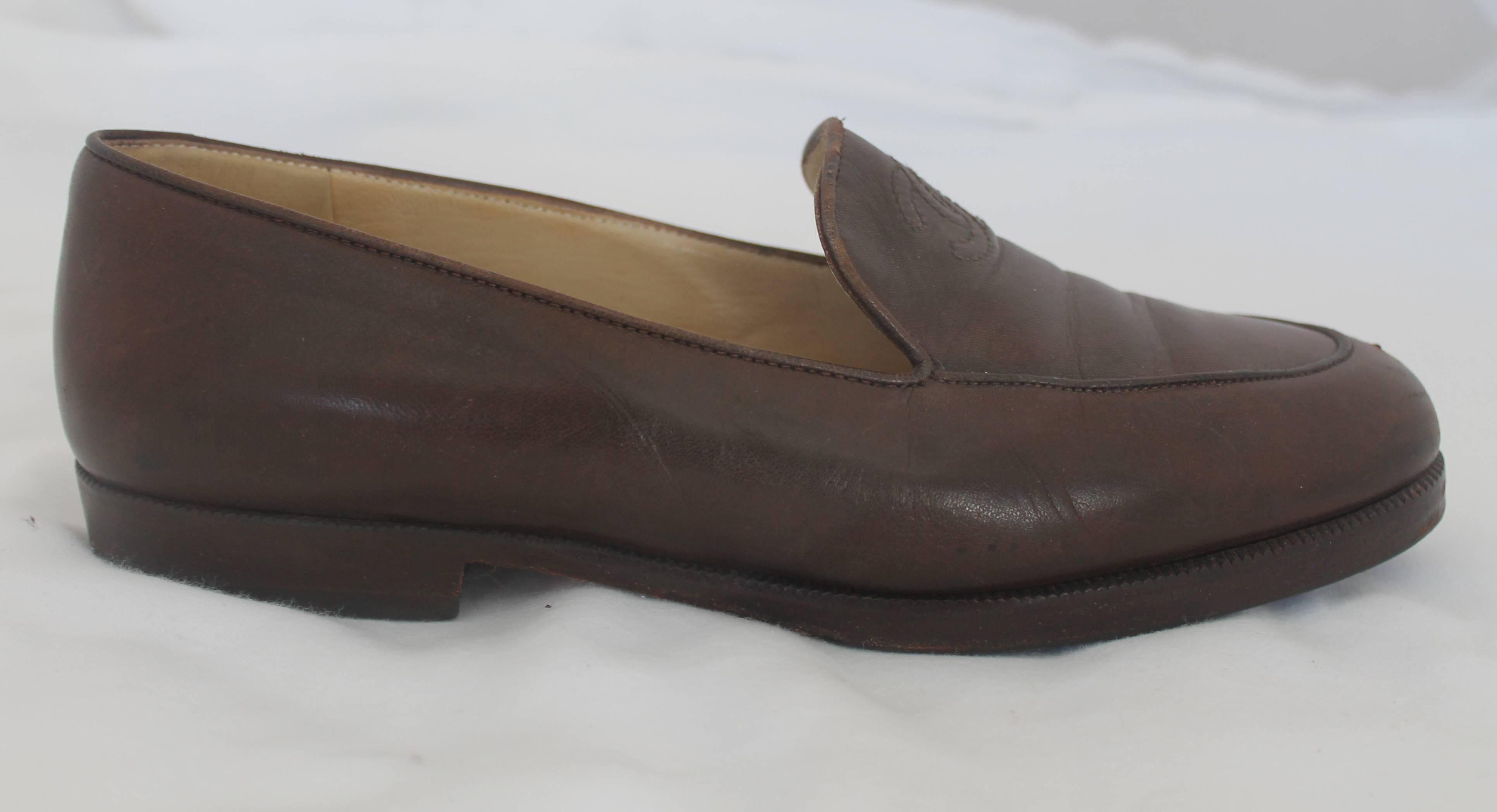 Chanel Brown Leather Loafers - 37. These brown loafers are made of leather and have the Chanel logo stitched into the top of the shoe. They are in good condition with minor wear on the inside and bottom. The front of each shoe show some