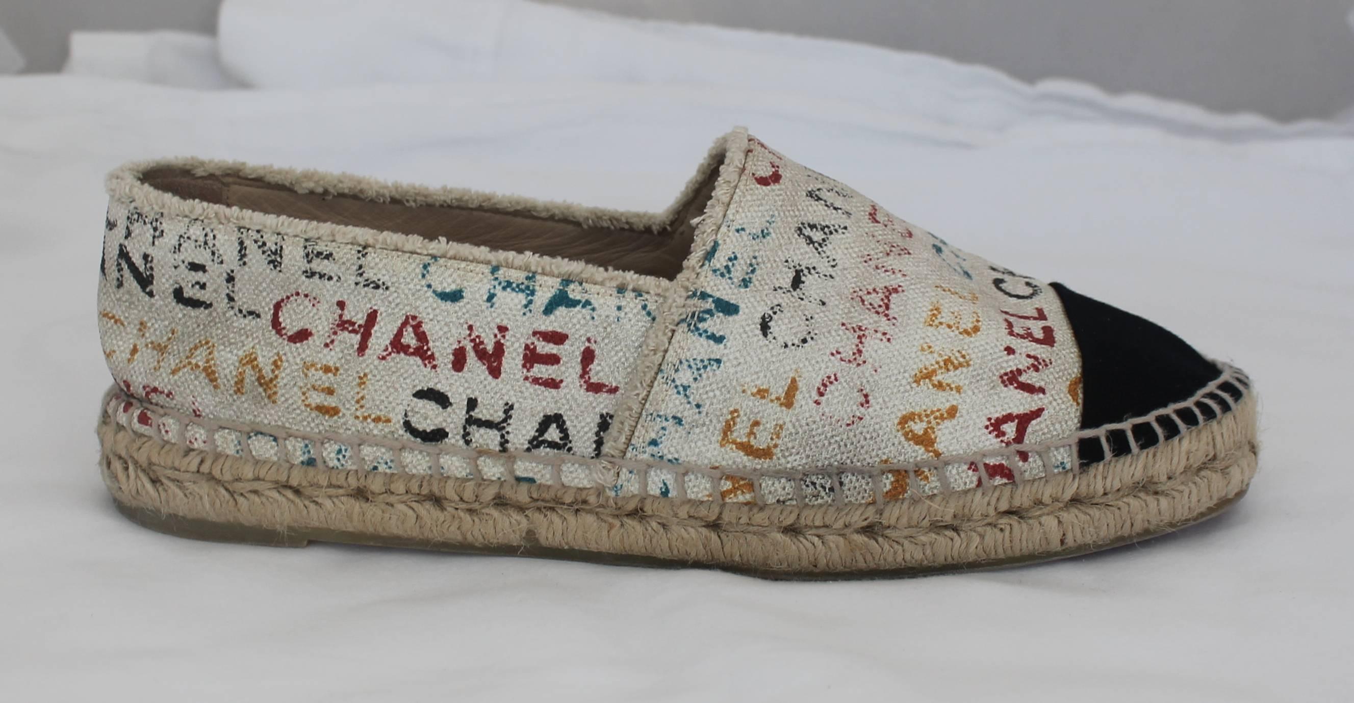 Chanel Black and Cream with Multi-Colored Print Flat Espadrilles - 41. These espadrilles are great for the summer! They are cream with a black toe and tan, rope material stitching. The cream part of the shoe is covered with the word 