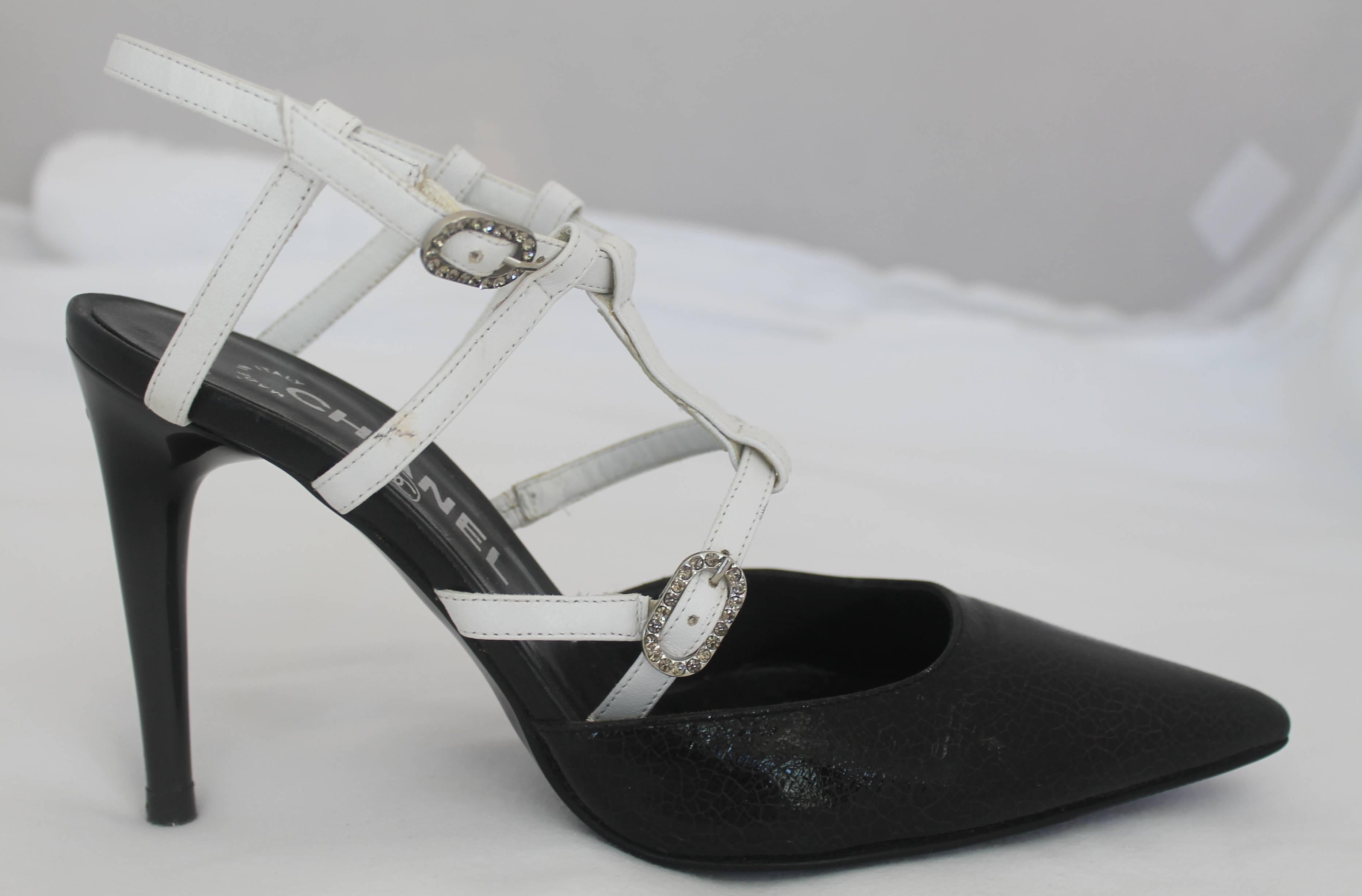 Chanel Black and White Cracked Patent Leather Pointed-Toe Heels - 35.5. These gorgeous heels are black cracked patent leather with white straps. Each shoe has two rhinestone buckles. At the top of each heel there is a silver metal Chanel logo. They