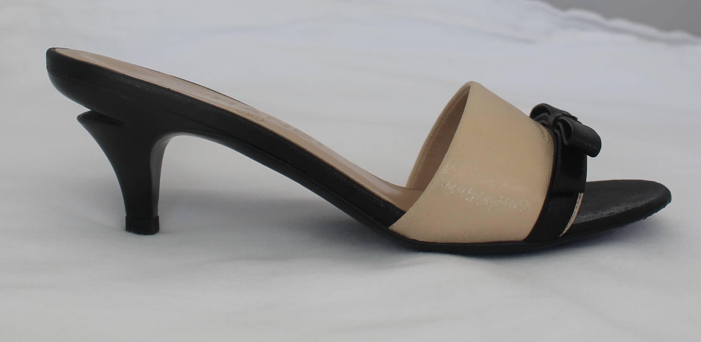 Chanel Tan and Black Leather Kitten Heels with Black Bow and Heel Cutout - 36. These classy kitten heels are tan and black and have a black leather bow on them. The bow also has a black Chanel logo charm on them. The black heel has a cutout near the