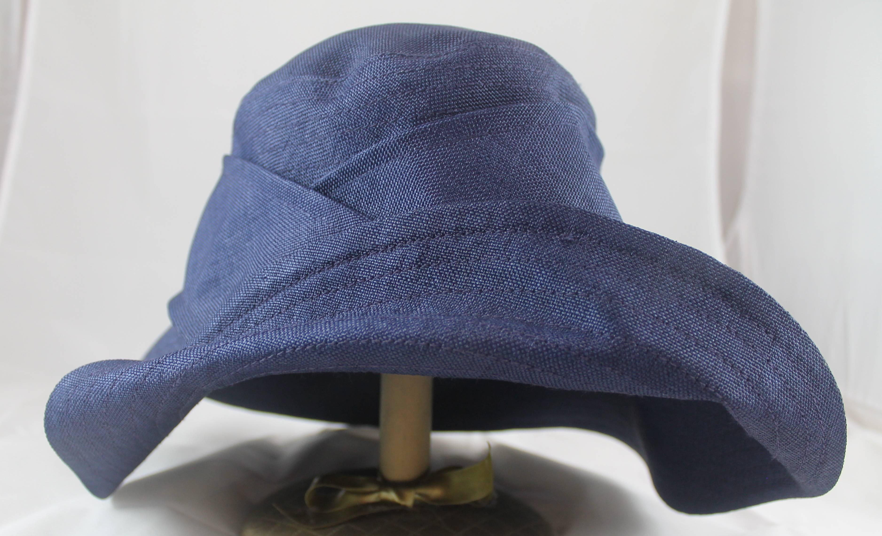 Suzanne Custom Millinery Navy Thin Raffia Hat with Buttons. This floppy fold over style hat has 2 front buttons. Half of the brim is folded up and connected to the center trim of the hat. It is in excellent condition.